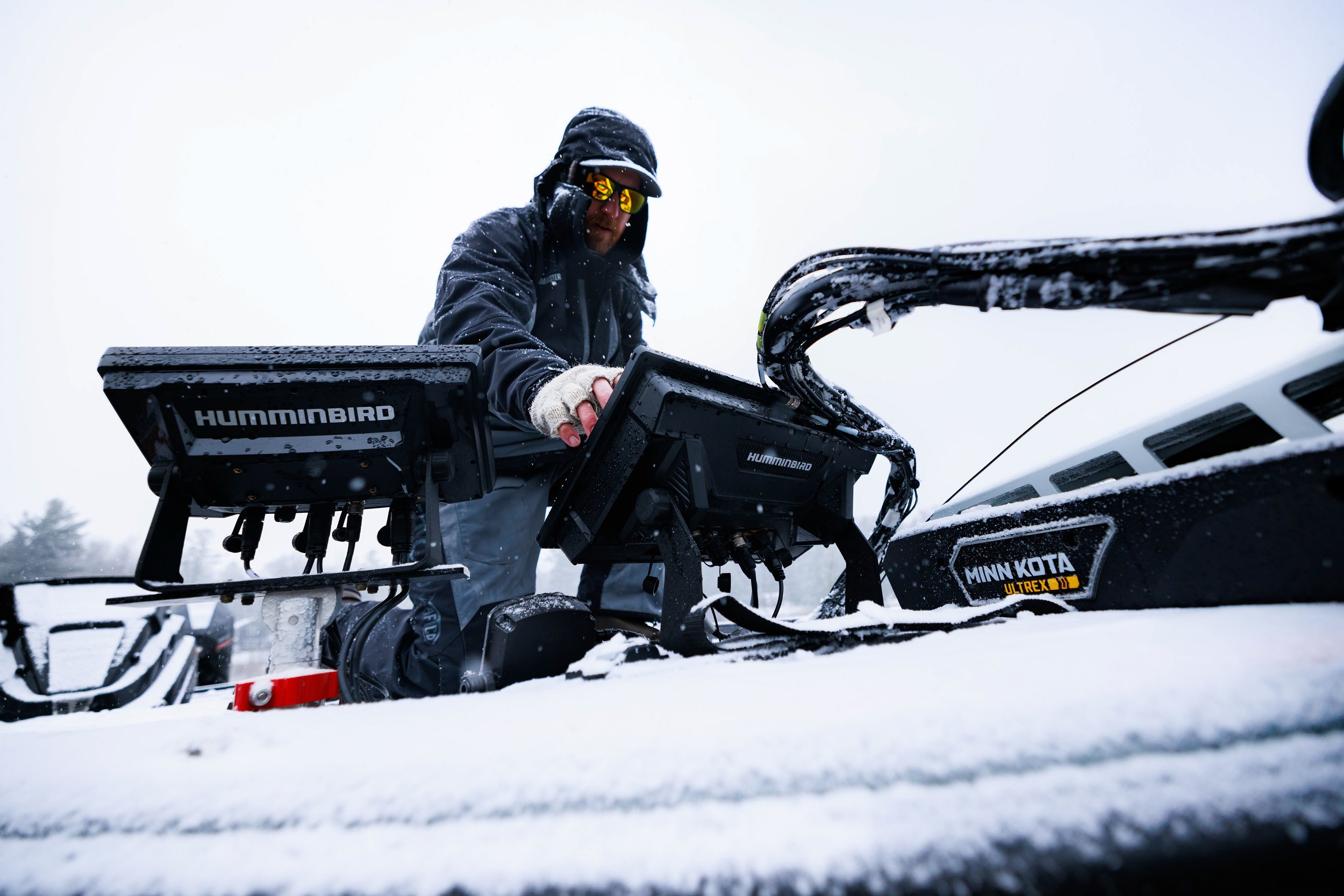 Person in winter gear operating a snowmobile with a Humminbird GPS device in snowy conditions.