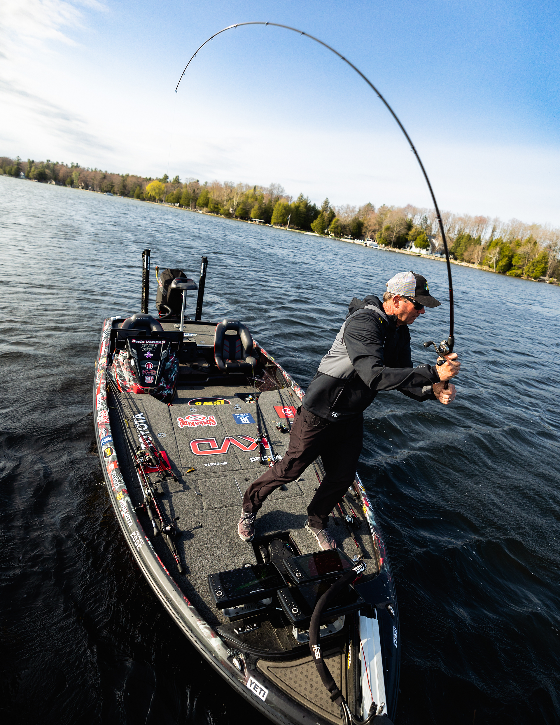 Man fishing from a boat on a lake under partly cloudy sky.