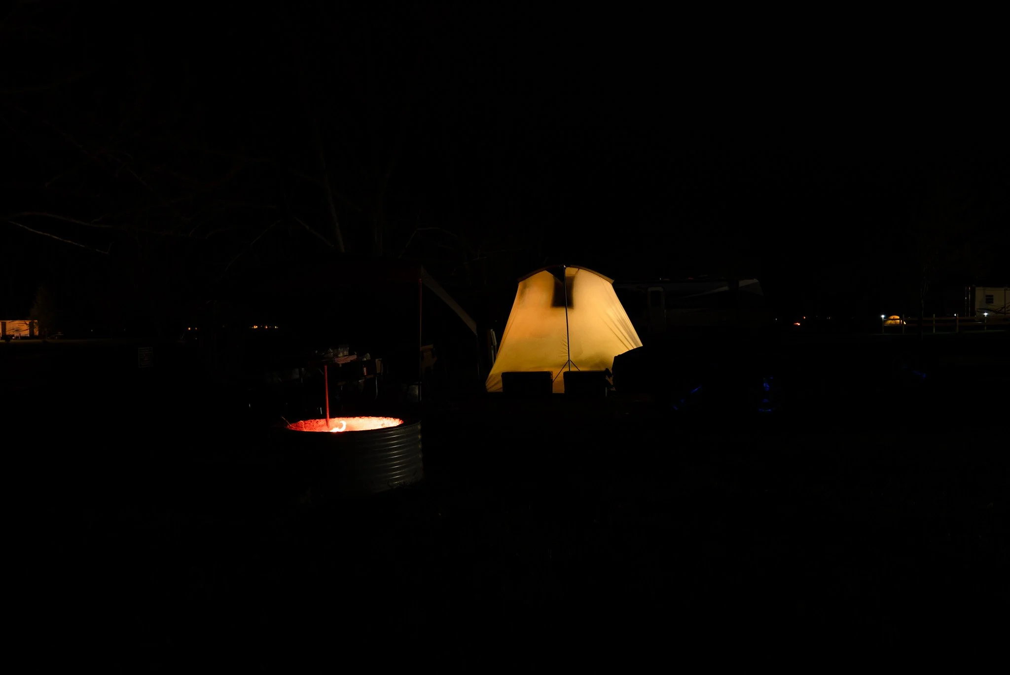 Nighttime camping scene with a glowing yellow tent and a campfire in a metal container.