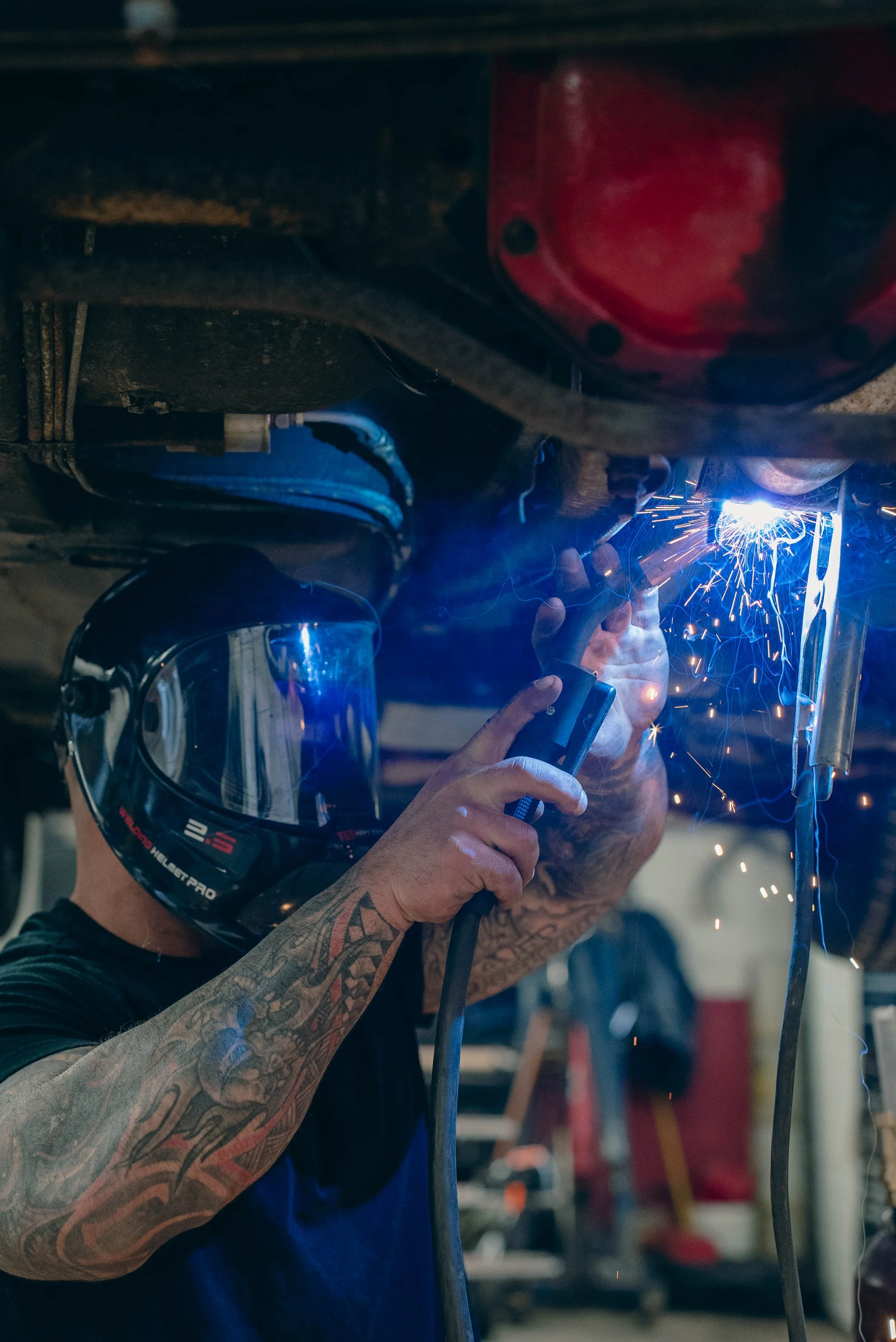 A person wearing a welding helmet and gloves welding metal, producing sparks.