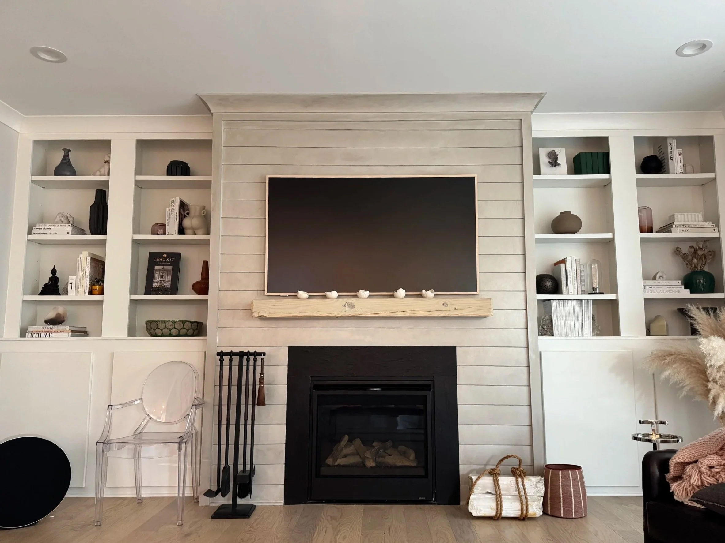 Living room with fireplace, mounted flat-screen TV above, and built-in white bookshelves filled with decorative items and books.