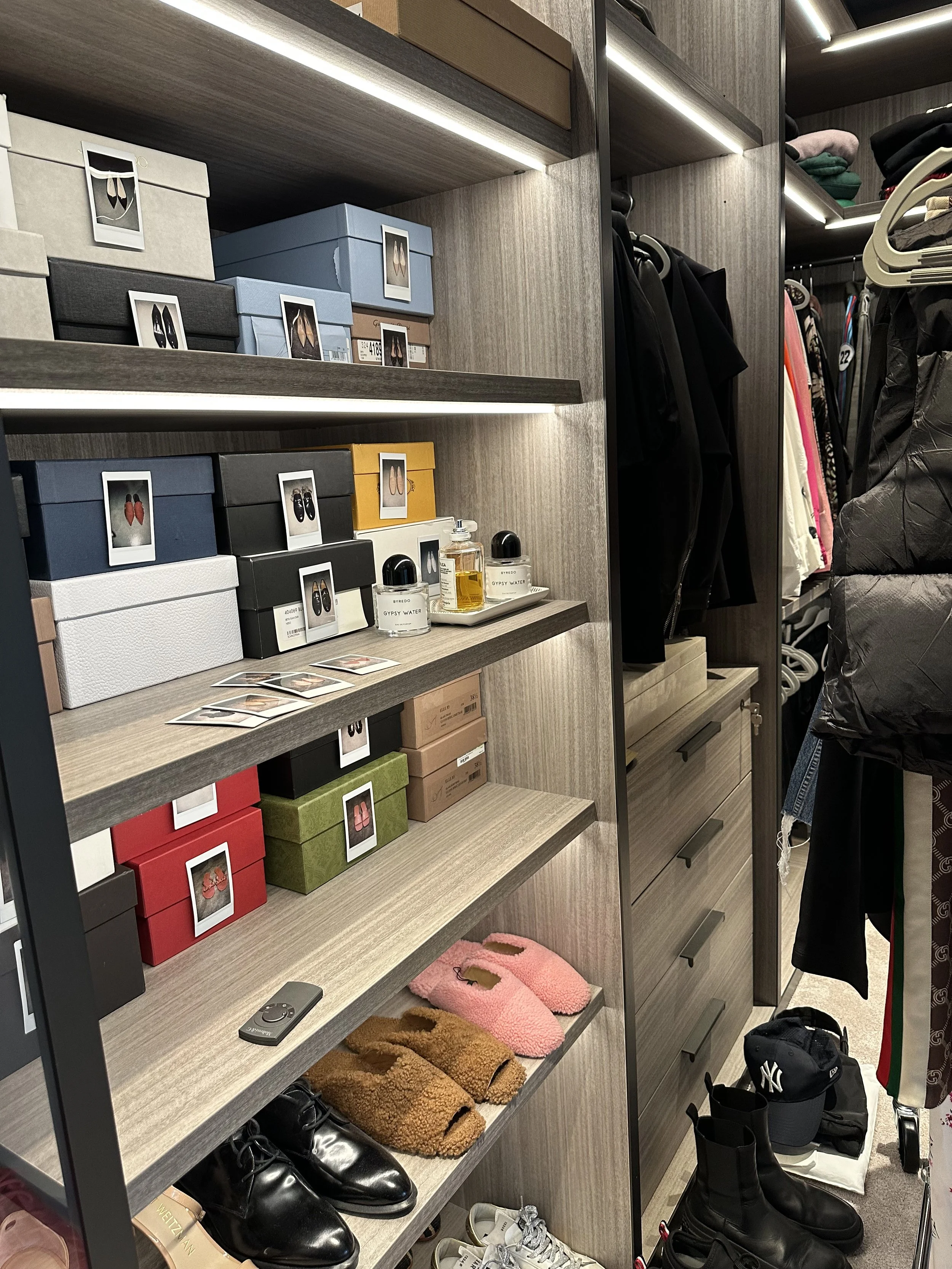 Display shelf with various boxes, perfume bottles, slippers, and shoes in a closet or retail space.