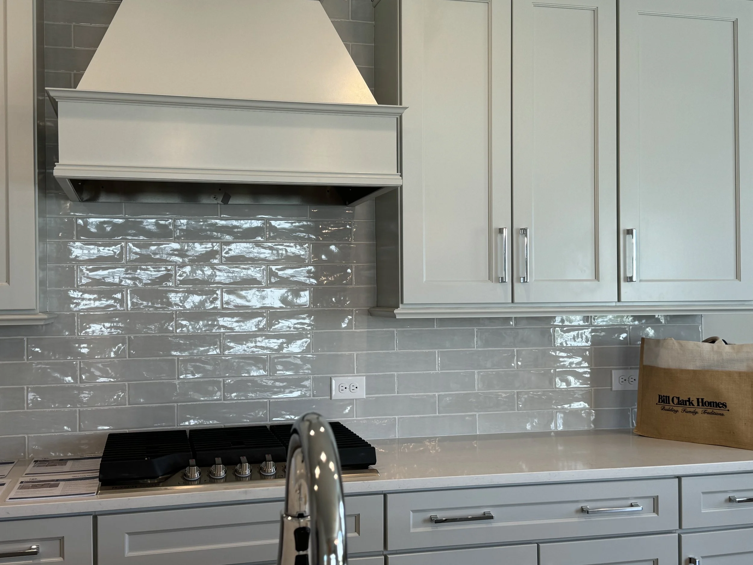 Modern kitchen with white cabinets, a beige countertop, a stovetop, and a glossy gray tile backsplash.