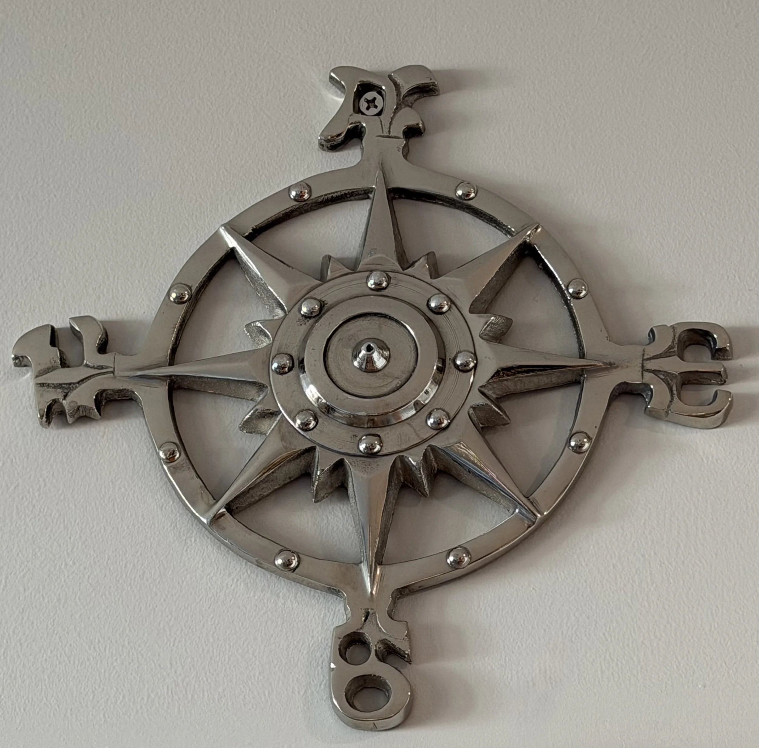 Metal wall decor in the shape of a pirate ship's steering wheel with a compass rose design.
