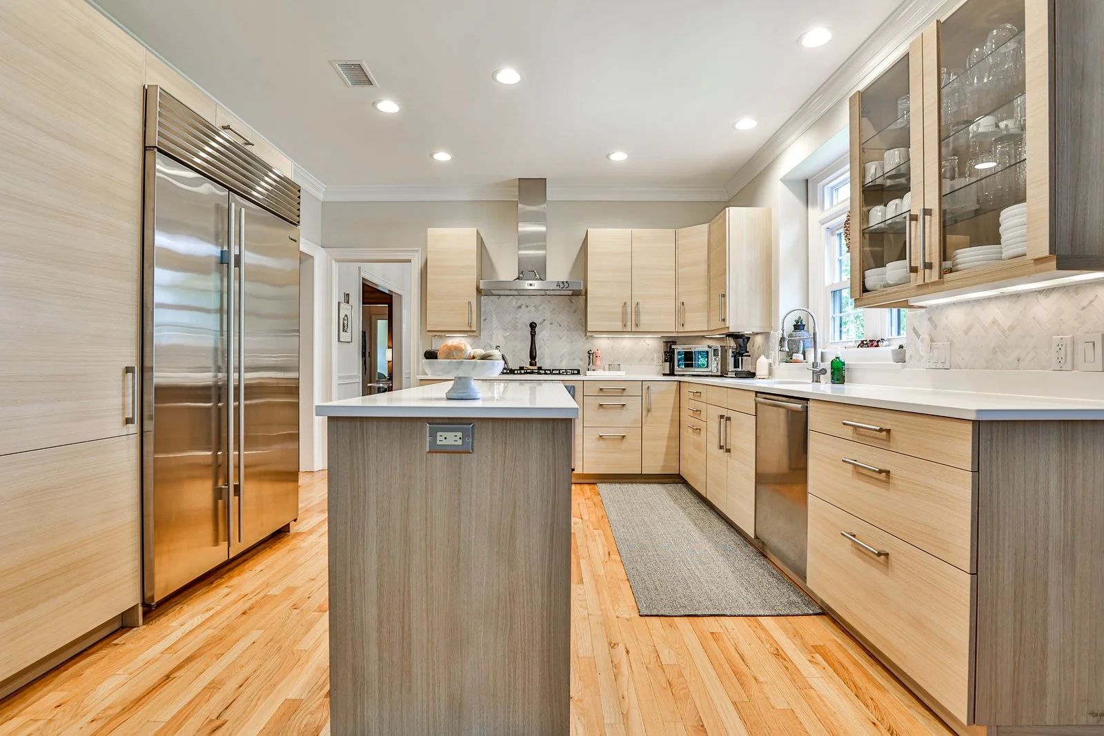 Modern kitchen with light wood cabinets, stainless steel appliances, marble backsplash, and hardwood flooring.
