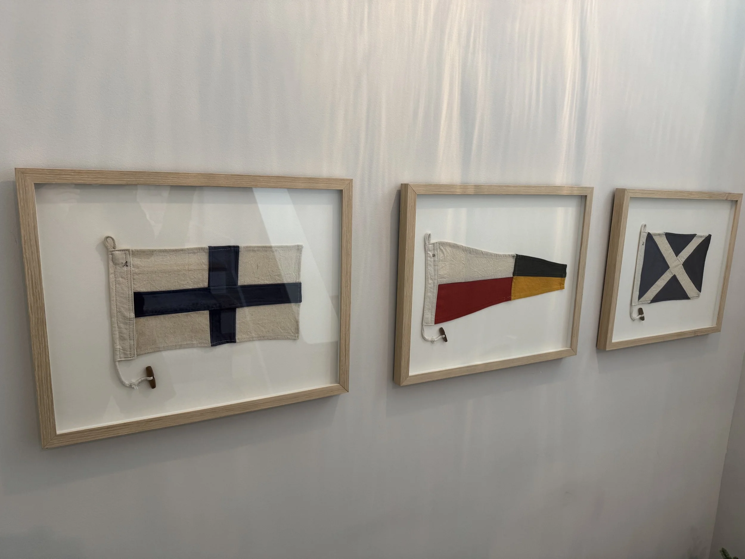 Three framed fabric flags mounted on a white wall, each with a small loop at the top left corner.