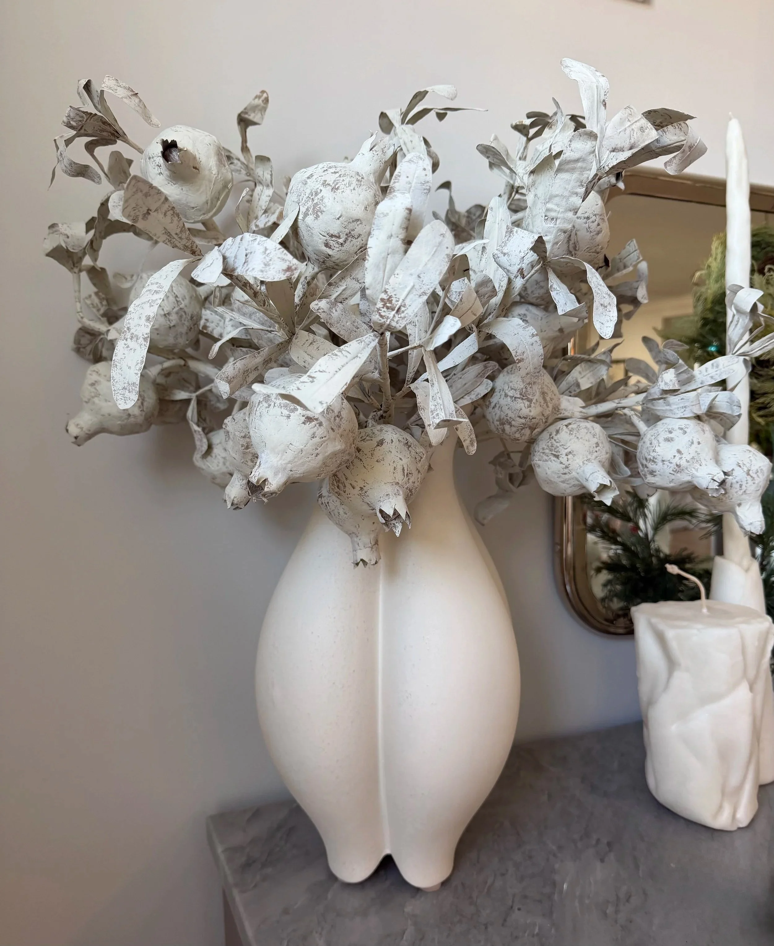 Decorative arrangement of eucalyptus branches in a cream-colored vase on a table.