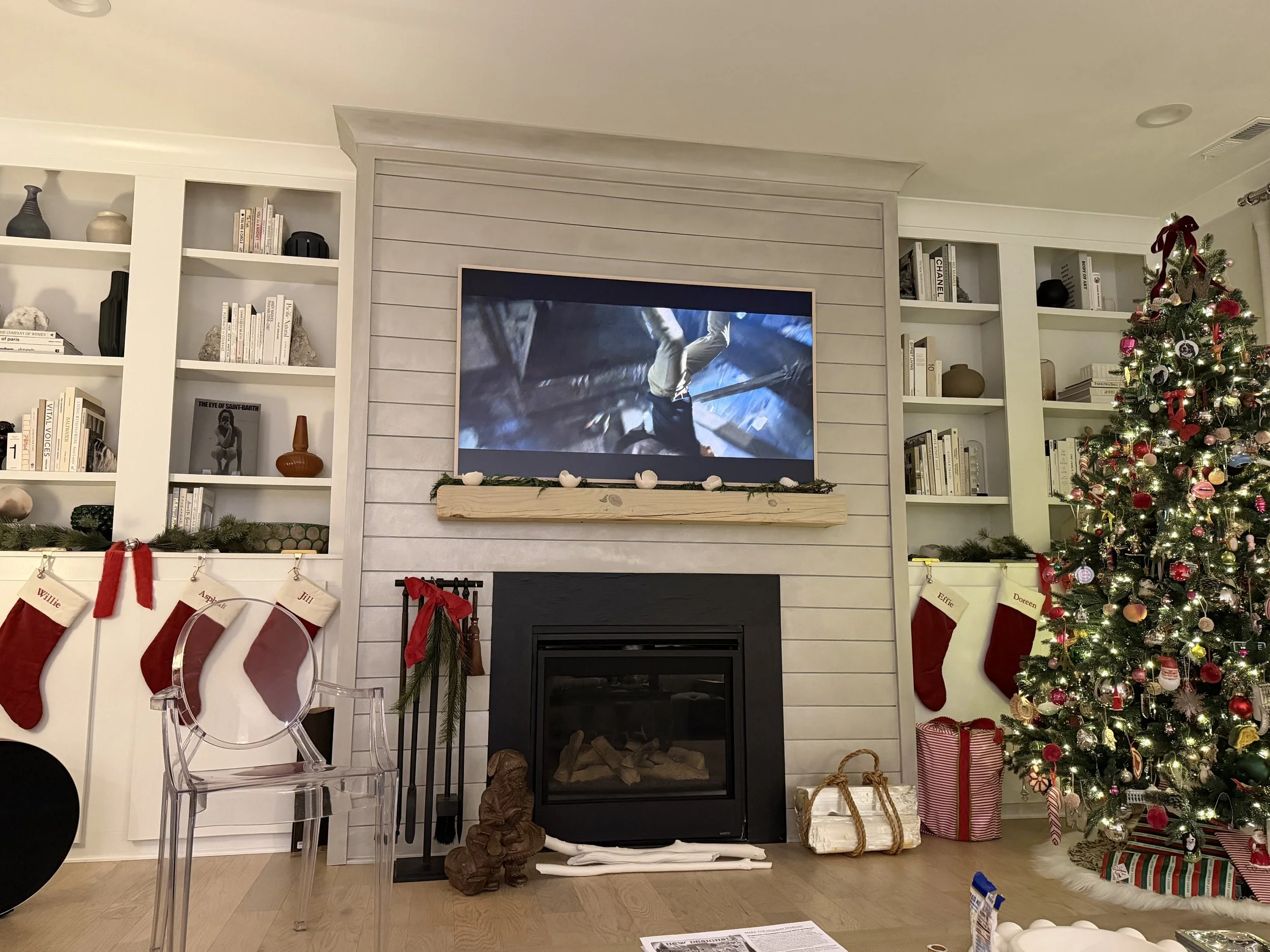 Living room decorated for Christmas with a tall decorated Christmas tree, stockings hanging on the fireplace, and wrapped presents on the floor.