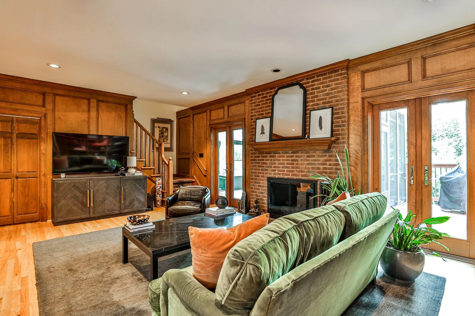 Living room with wooden cabinetry, a brick fireplace, green sofa, black coffee table, potted plant, and sliding glass doors.