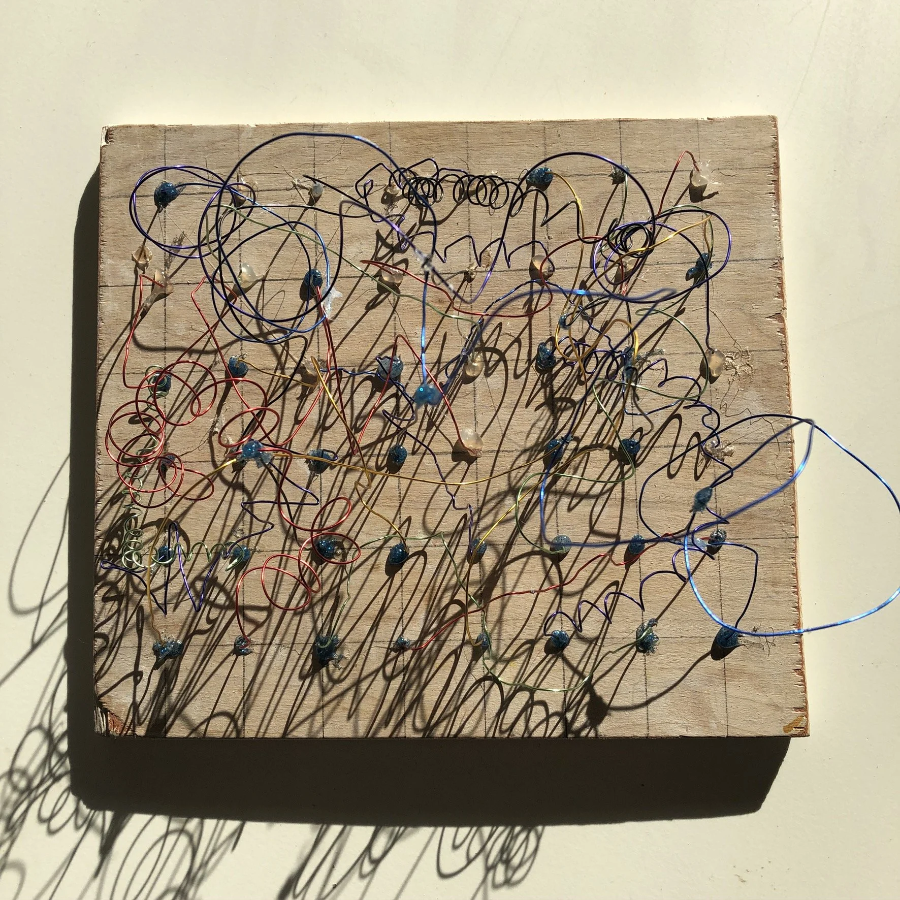A wooden board with colorful wires and pins arranged to create a shadow sculpture.