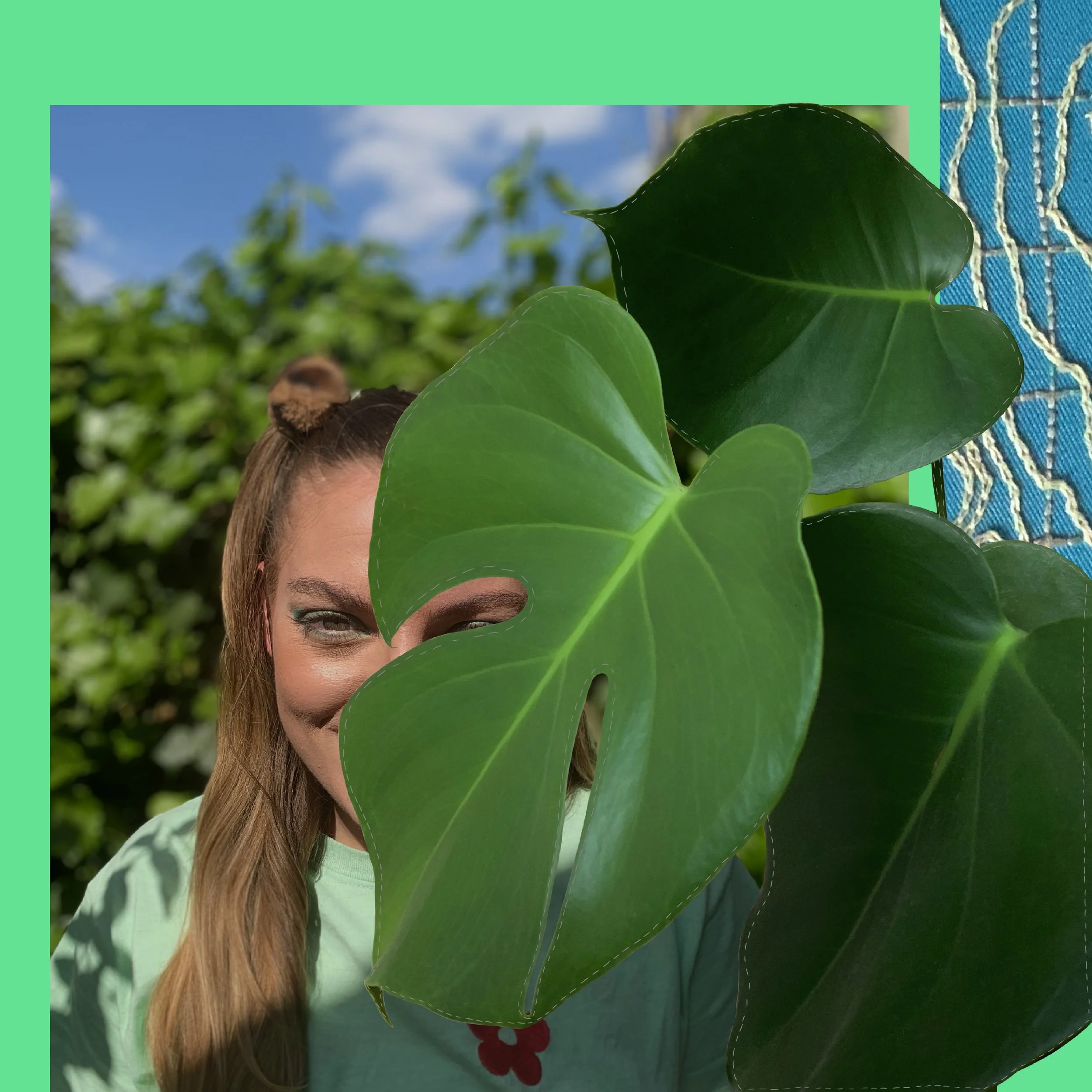A person outdoors with a large green leaf partially covering their face, smiling, with a background of blue sky and greenery.