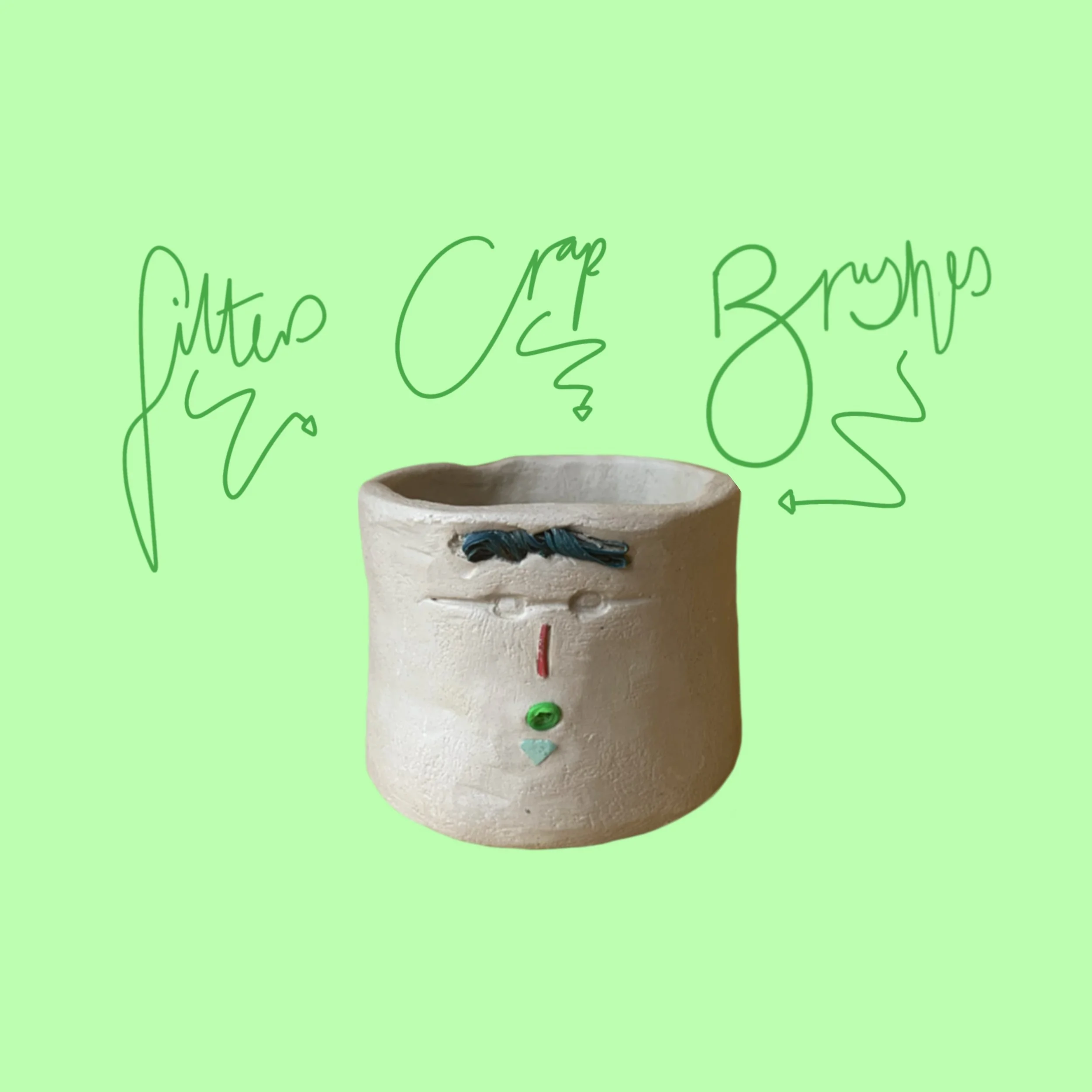 A ceramic pot with inlaid materials found on the beach arranged to resemble a face with blue hair, glasses (carved), a red nose and a green mouth in an o shape. Script writing with arrows. 