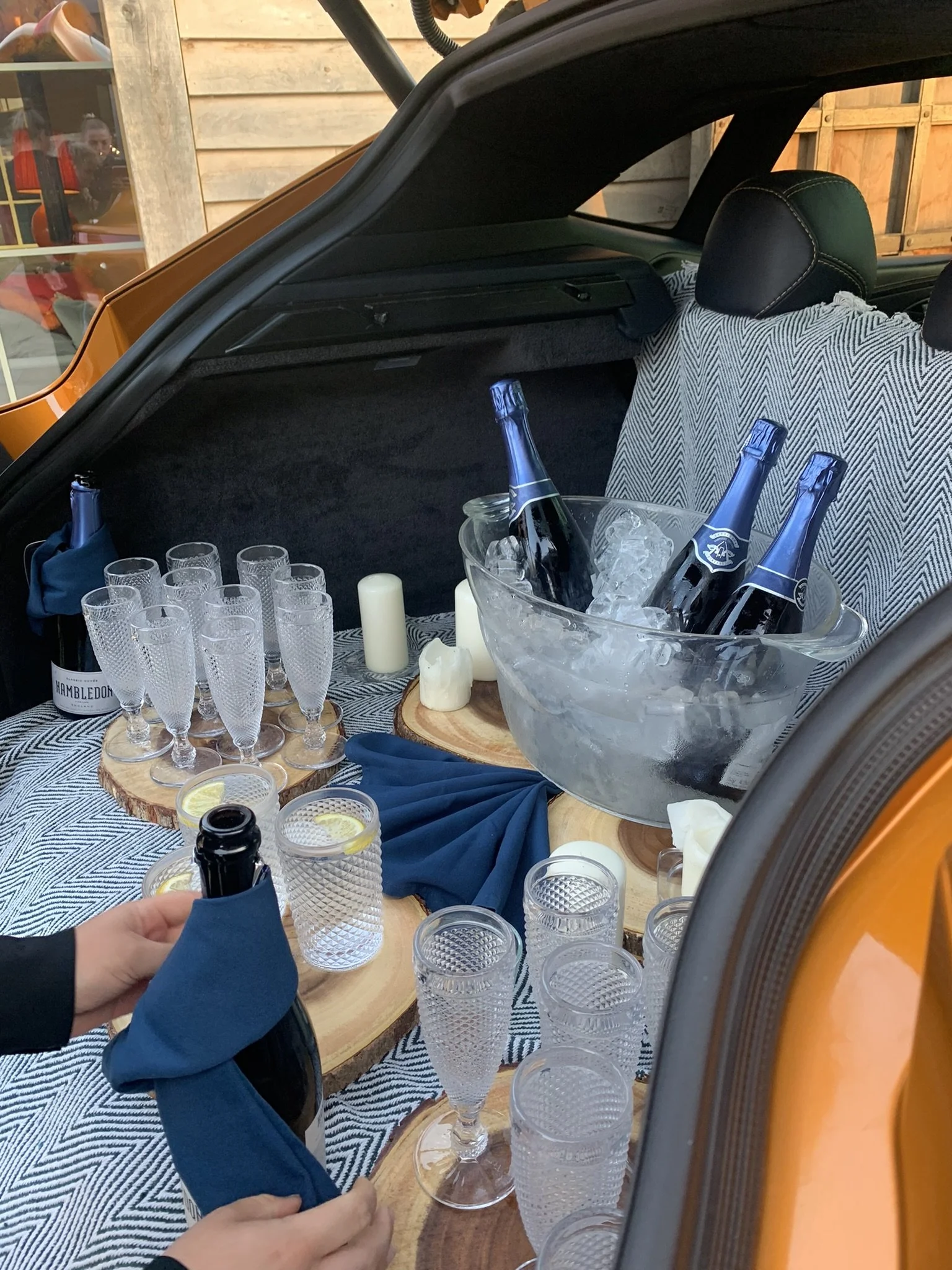 Back of a car trunk set up for a celebration with champagne bottles, glasses, candles, and decorative items.