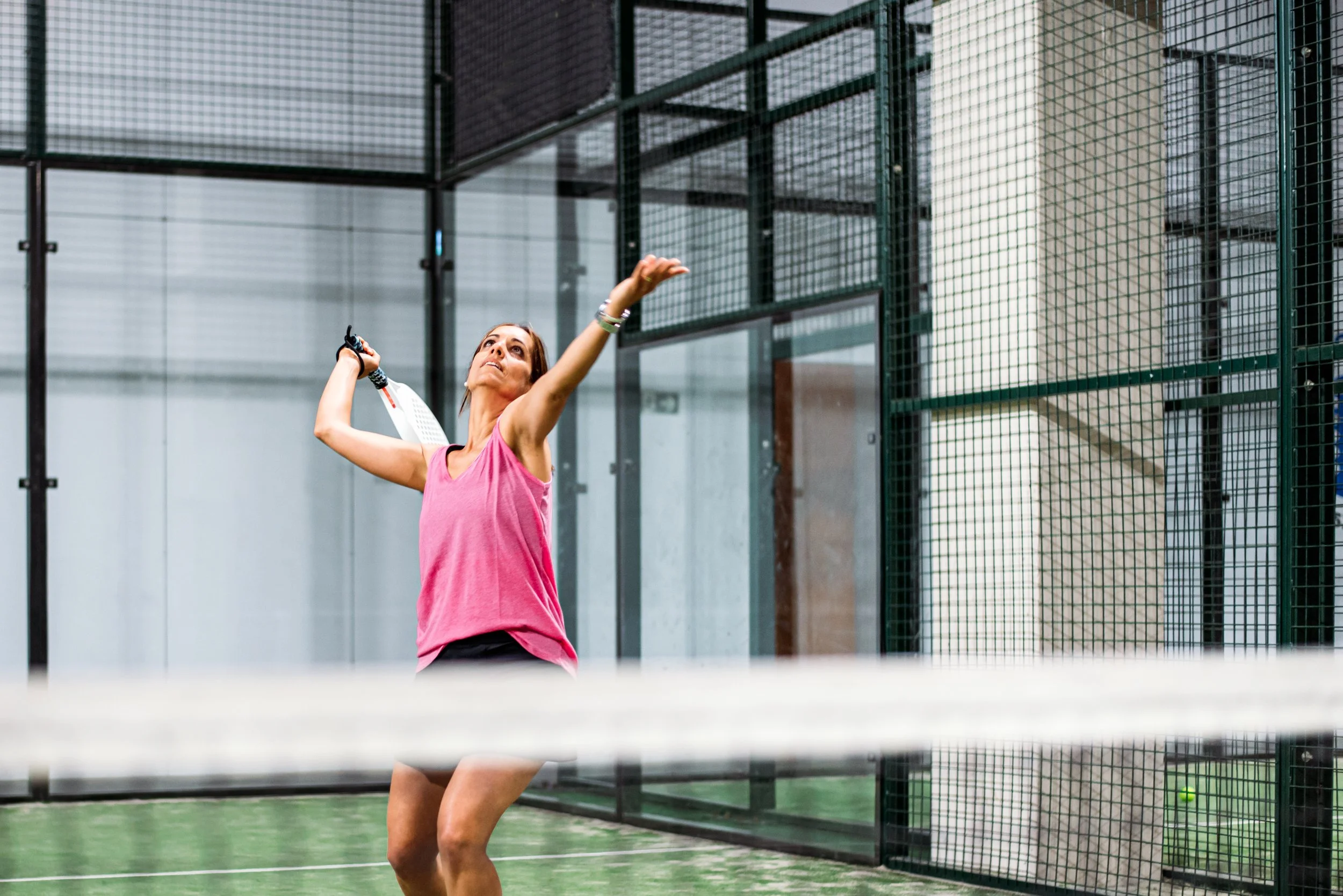 A woman playing a game of padel on an indoor court, preparing to hit the ball with her racket.