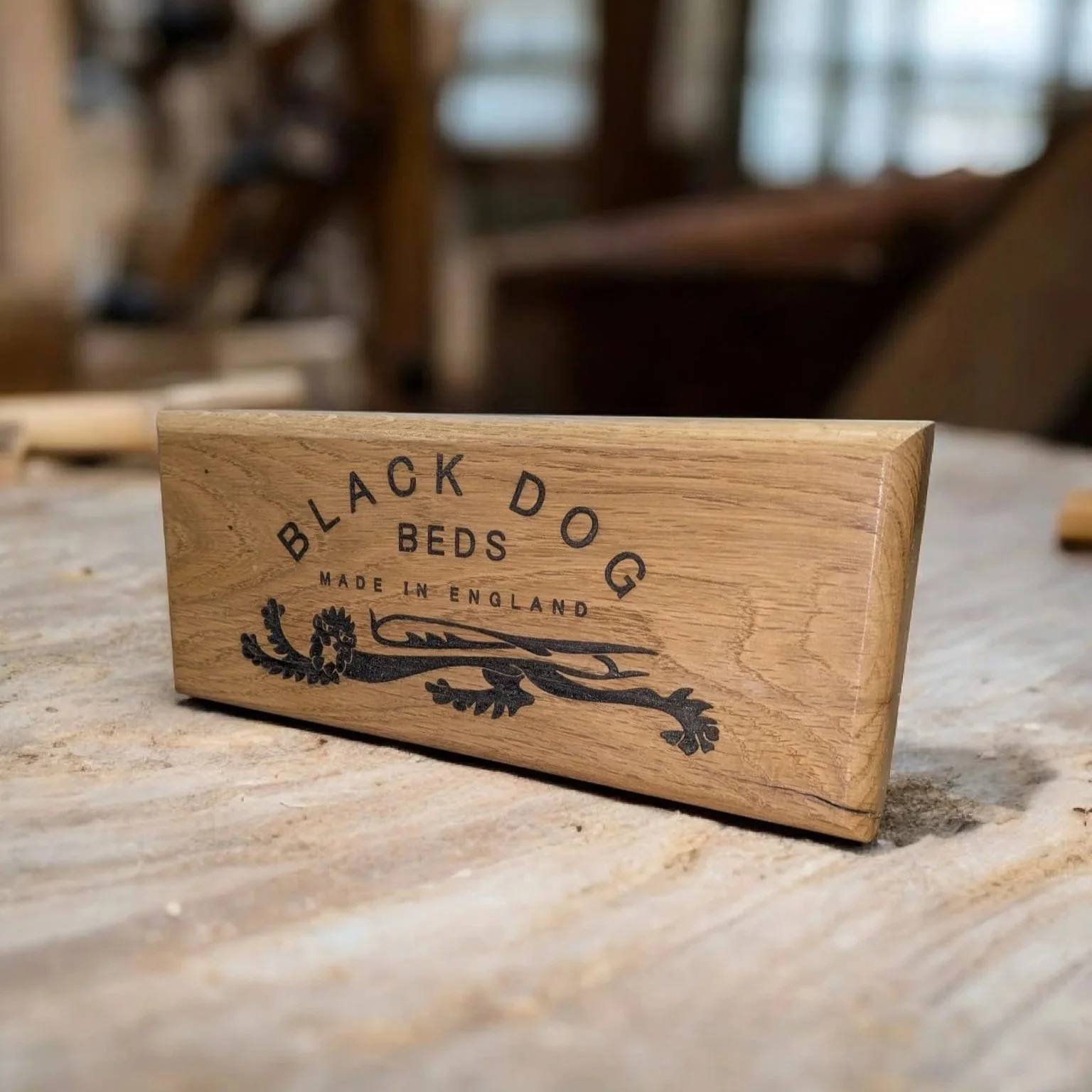 Wooden block with black text and design reading 'Black Dog Beds Made in England' placed on a wooden surface.