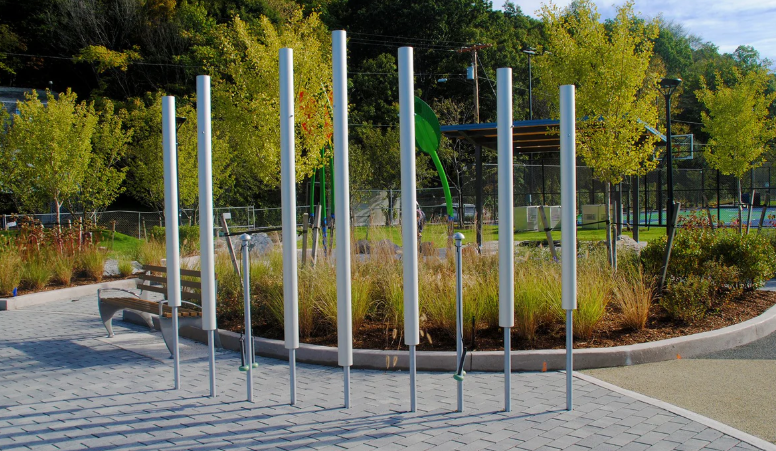 Park playground with tall white poles, benches, and surrounding greenery in autumn.