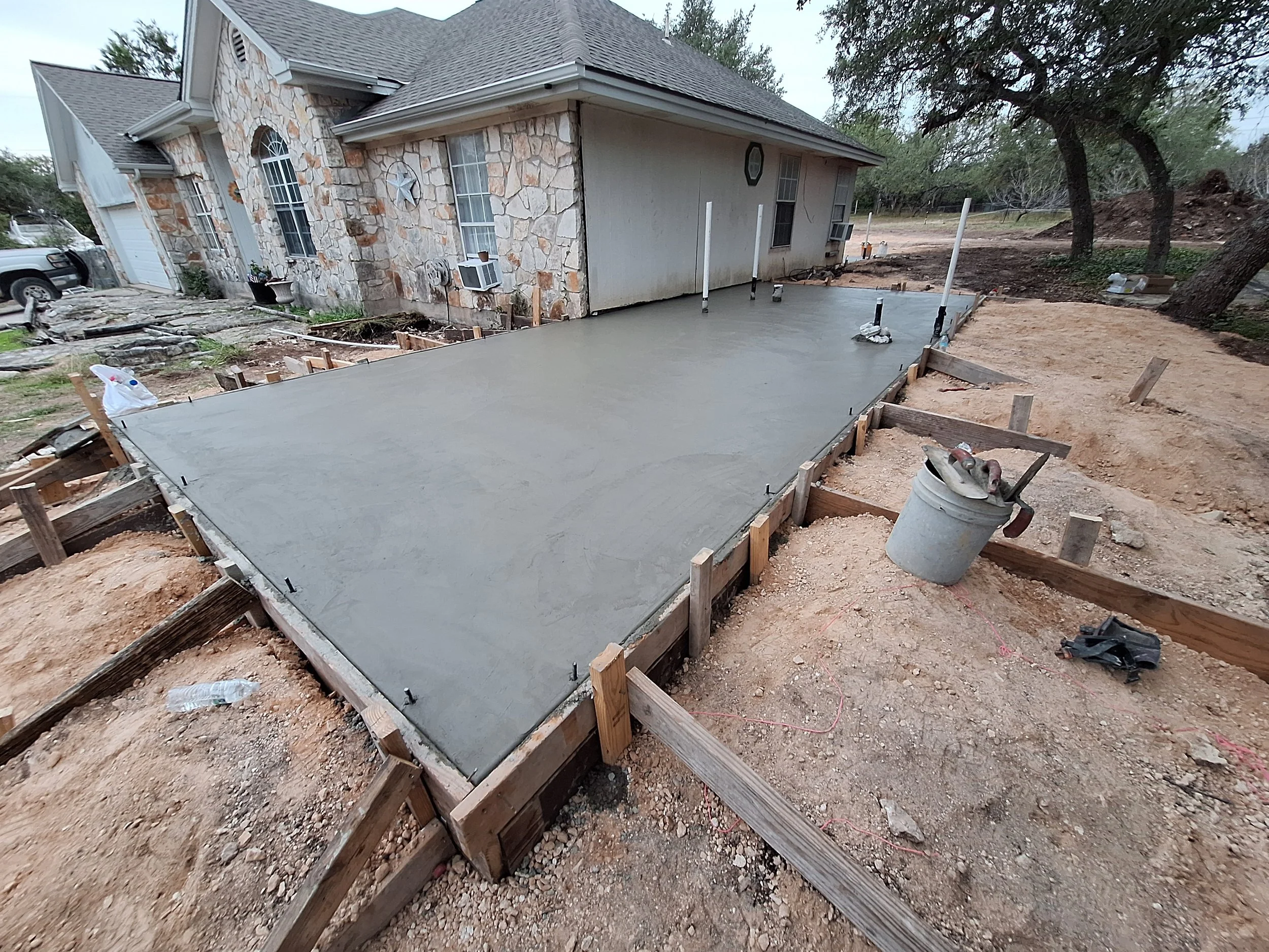 Concrete slab being poured for a new patio or extension in the backyard of a house, with wooden framing and construction tools and materials on site.