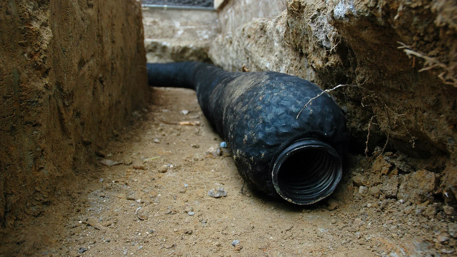 A black underground cable pipe lying on the ground between two dirt walls.