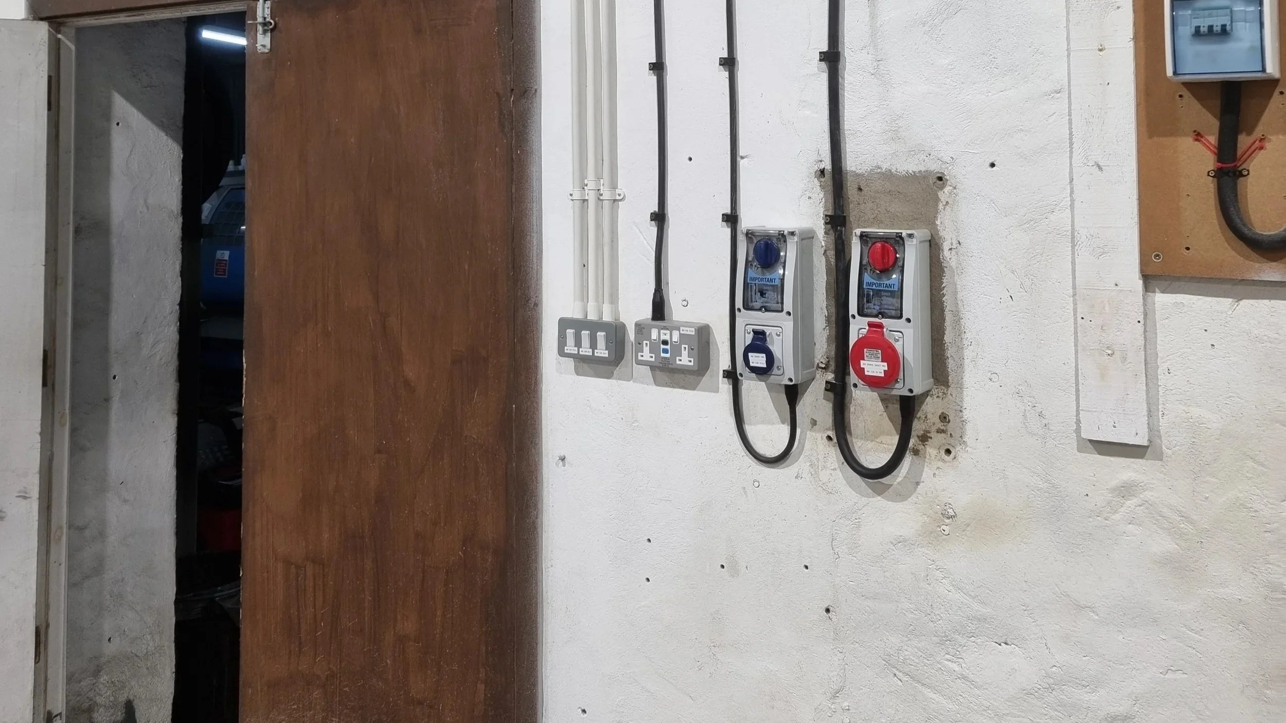Electrical outlets, switches, and power supplies mounted on a wall near a door in an industrial or utility room.