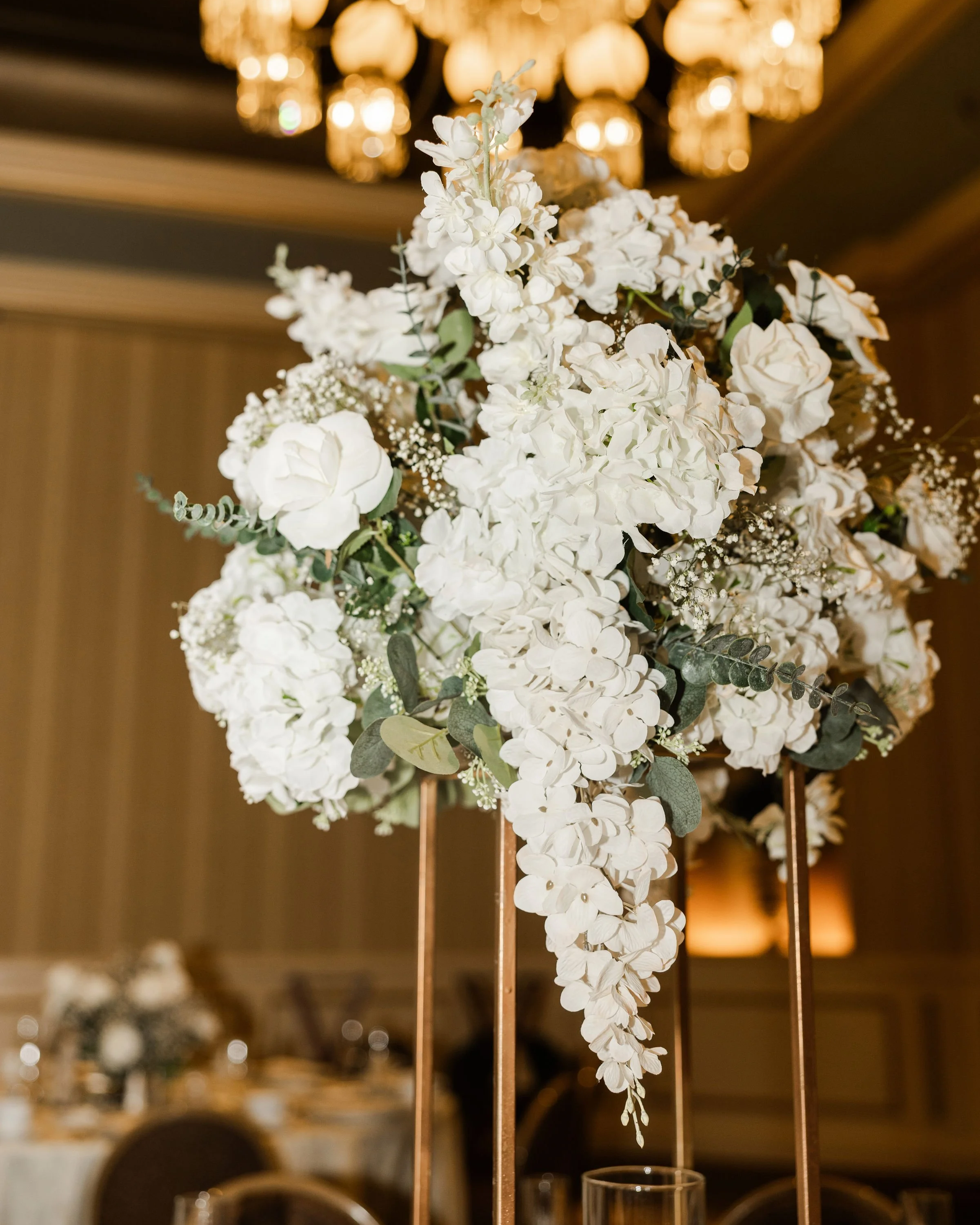 Elegant tall floral centerpiece with white flowers and greenery on a copper stand at a formal event