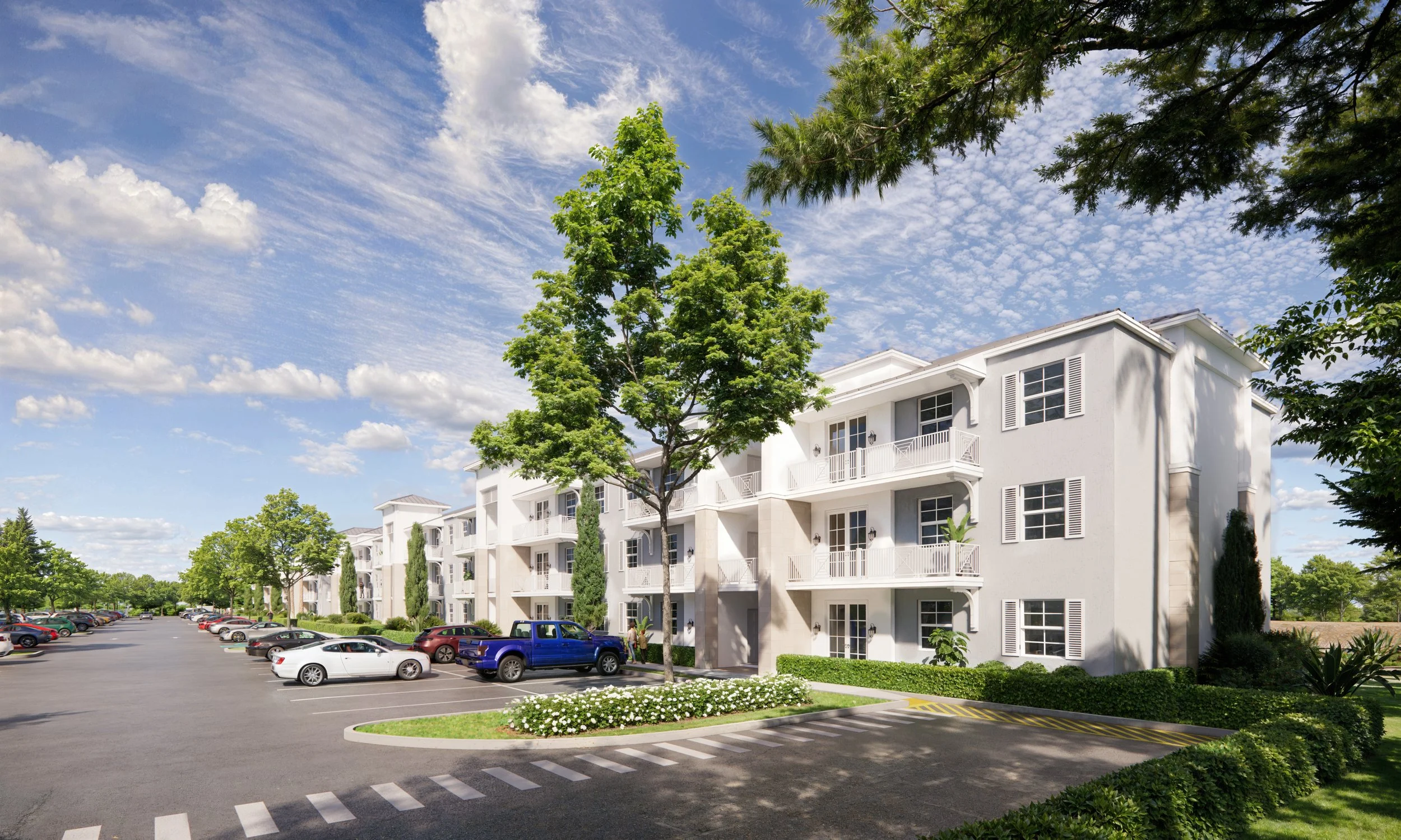 Exterior view of a white residential apartment complex with balconies, trees, a parking lot with cars, and a blue sky with clouds.