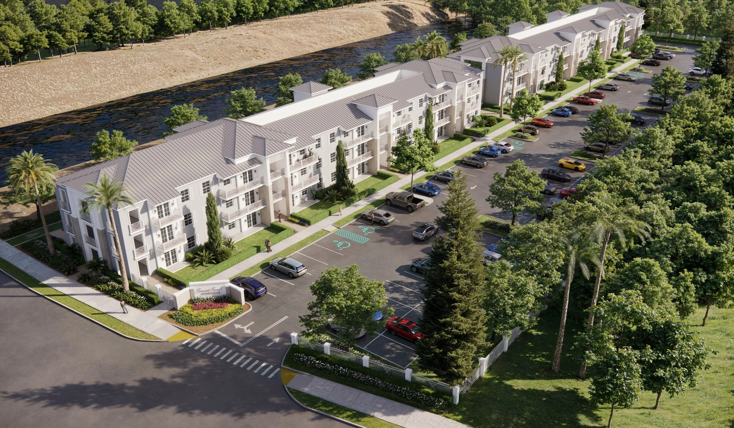 Aerial view of a residential apartment complex with parking lot, landscaping, and a nearby water body surrounded by trees.