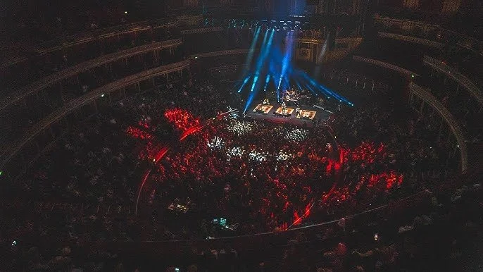 Concert venue with a stage illuminated by blue lights and a large crowd of people watching.