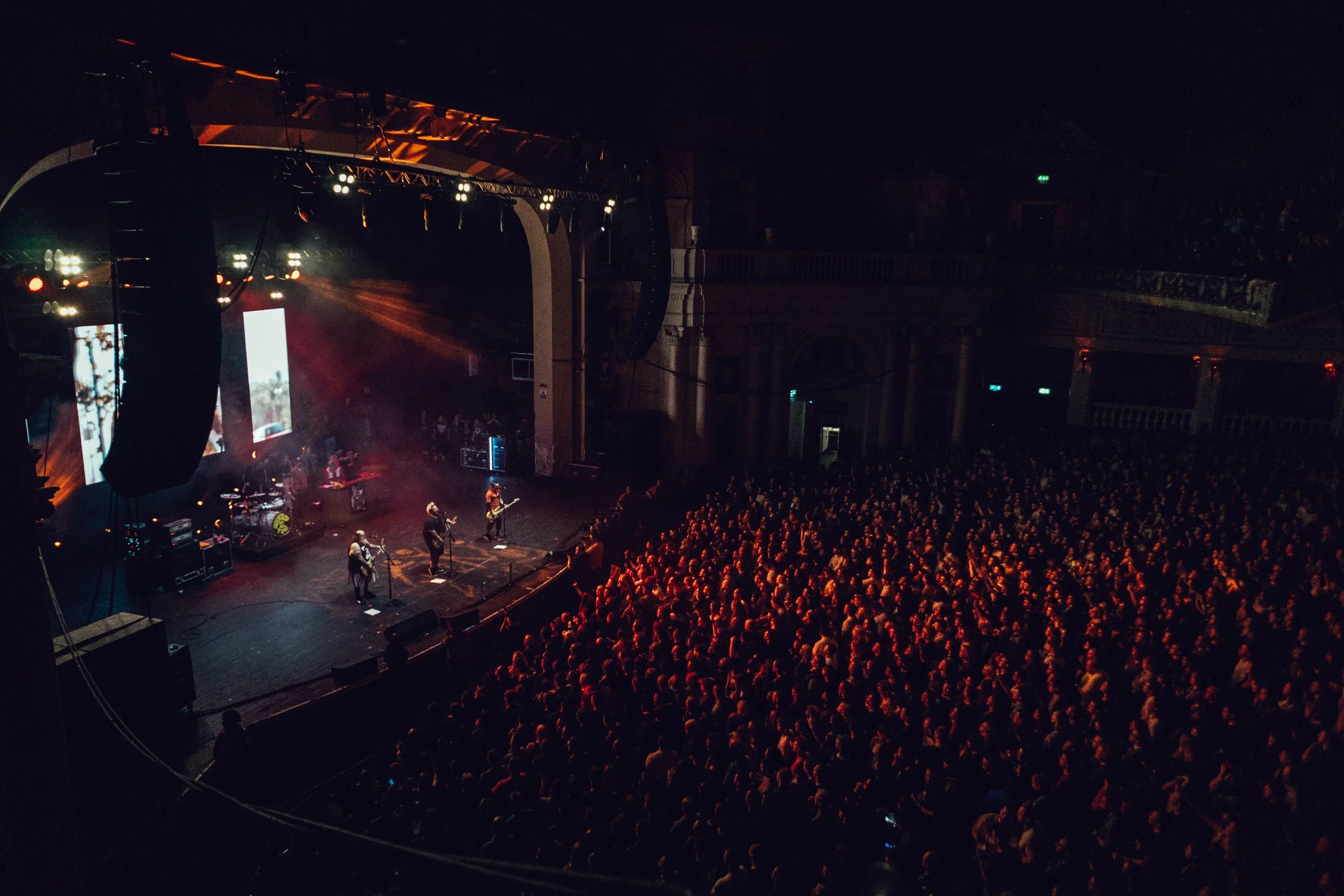 Concert hall with band performing on stage and large audience watching.