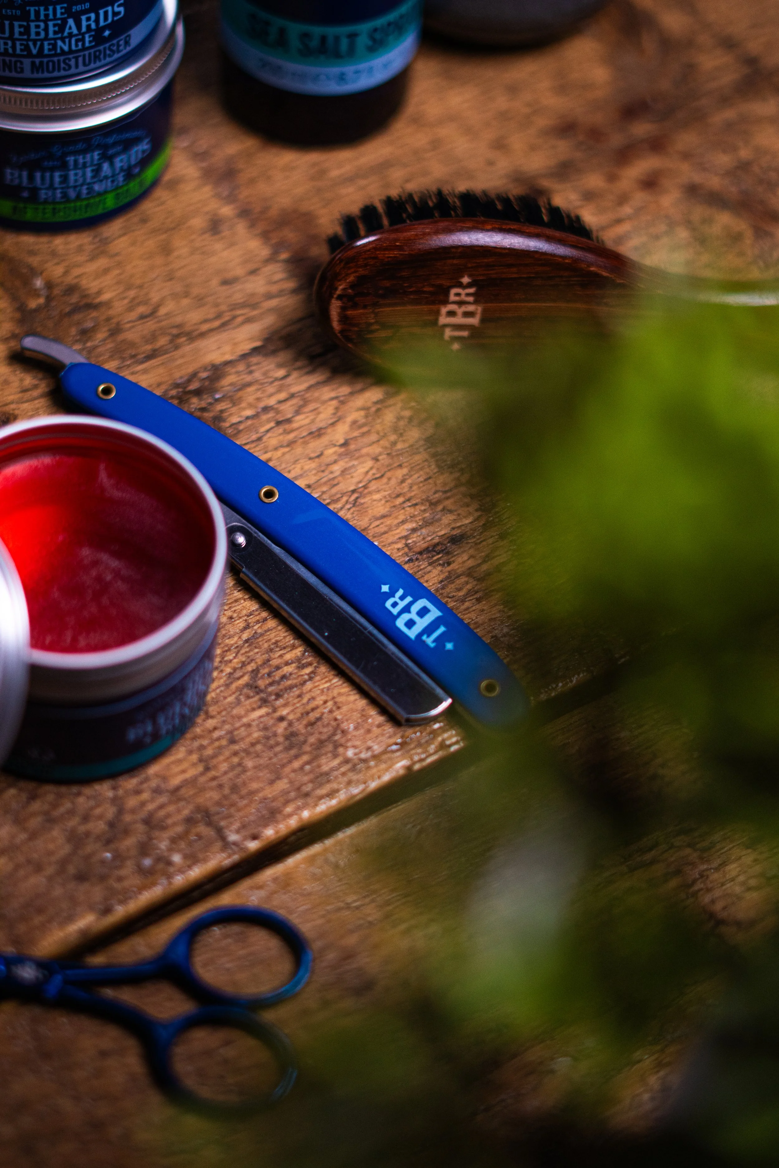 Barber tools and products on a wooden surface, including a blue straight razor with the label 