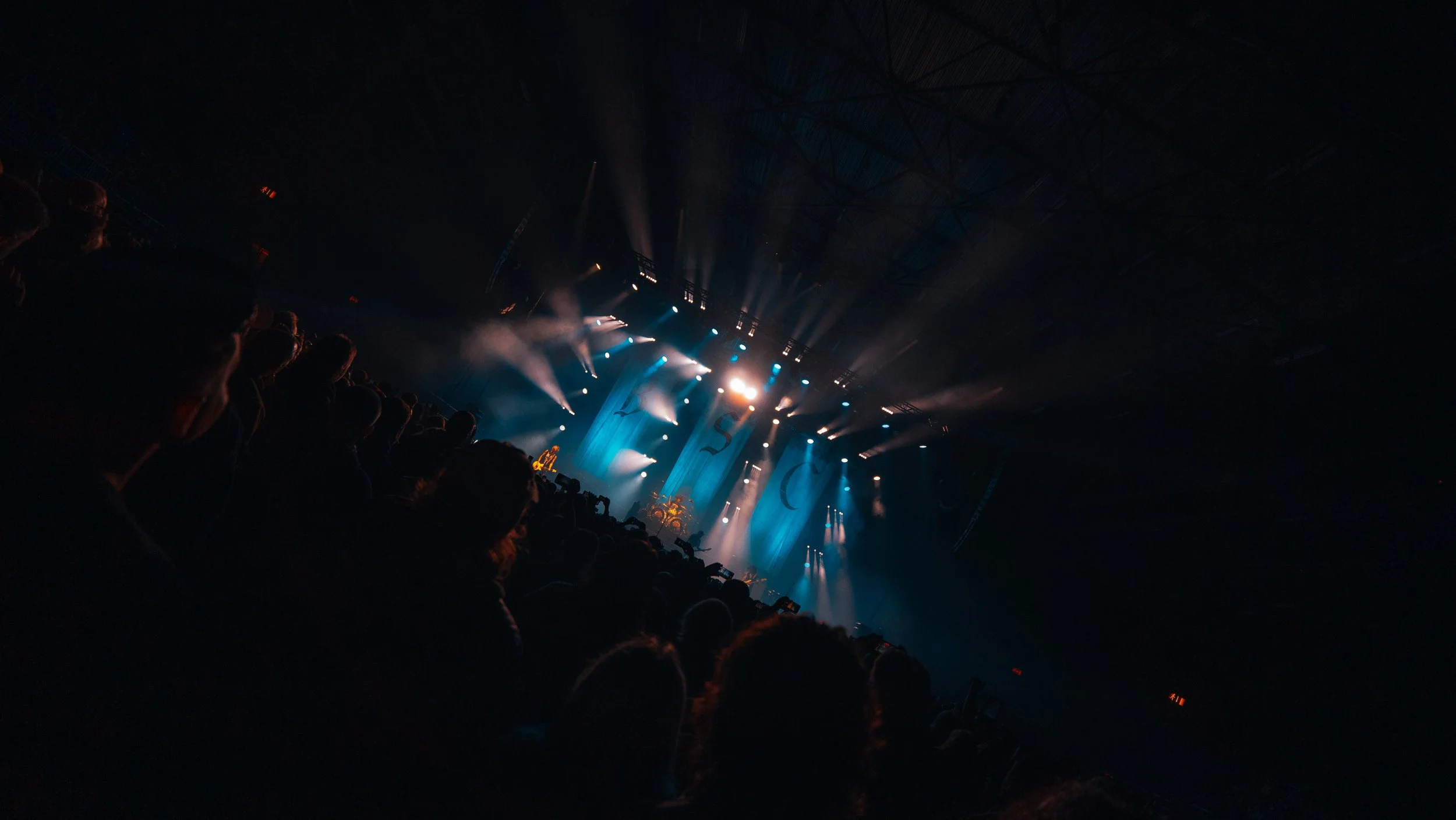 Concert crowd watching a brightly lit stage with performers and large curtains.
