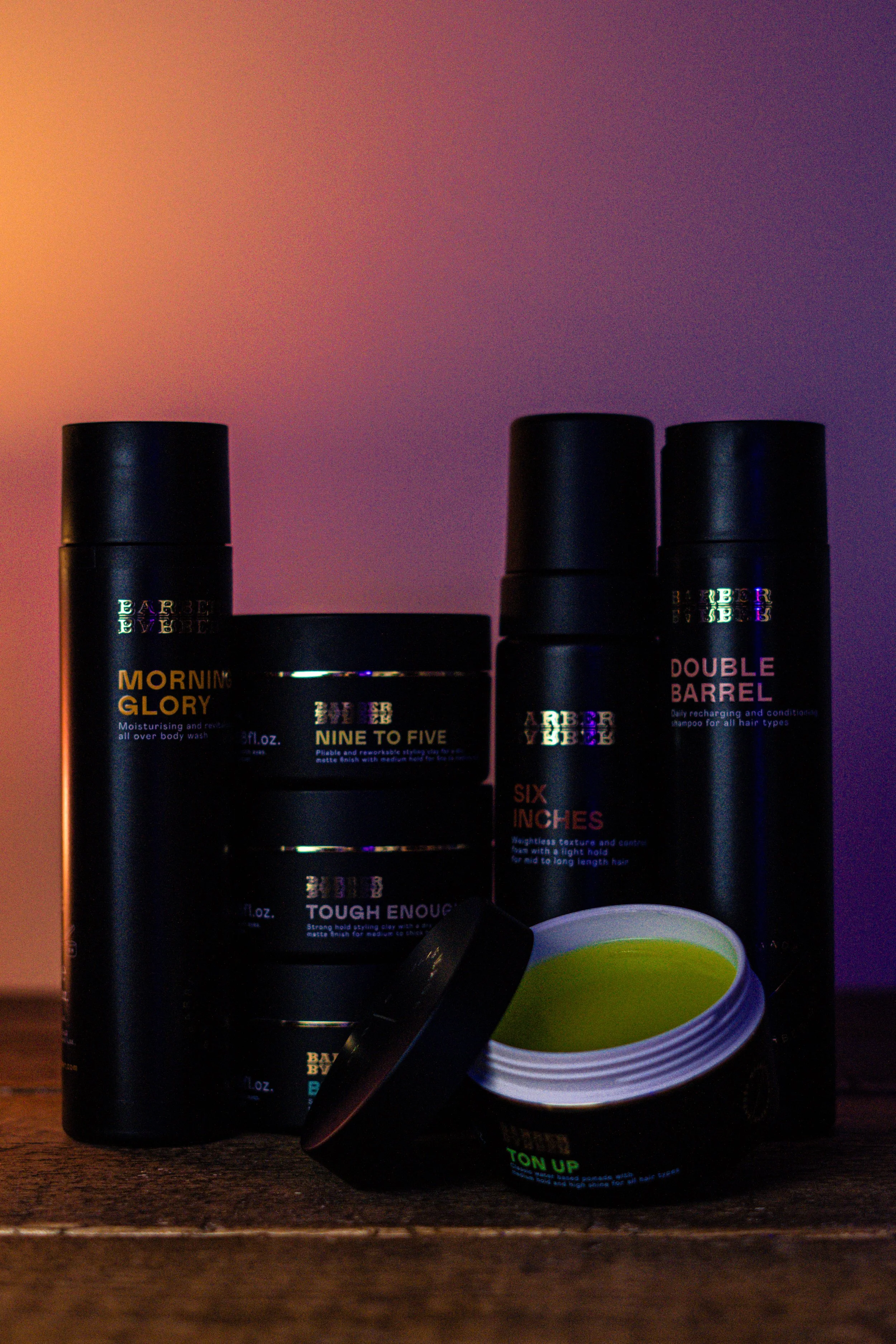 Collection of men's grooming products, including body wash, beard balm, and styling cream, on a wooden surface with a colorful gradient background.