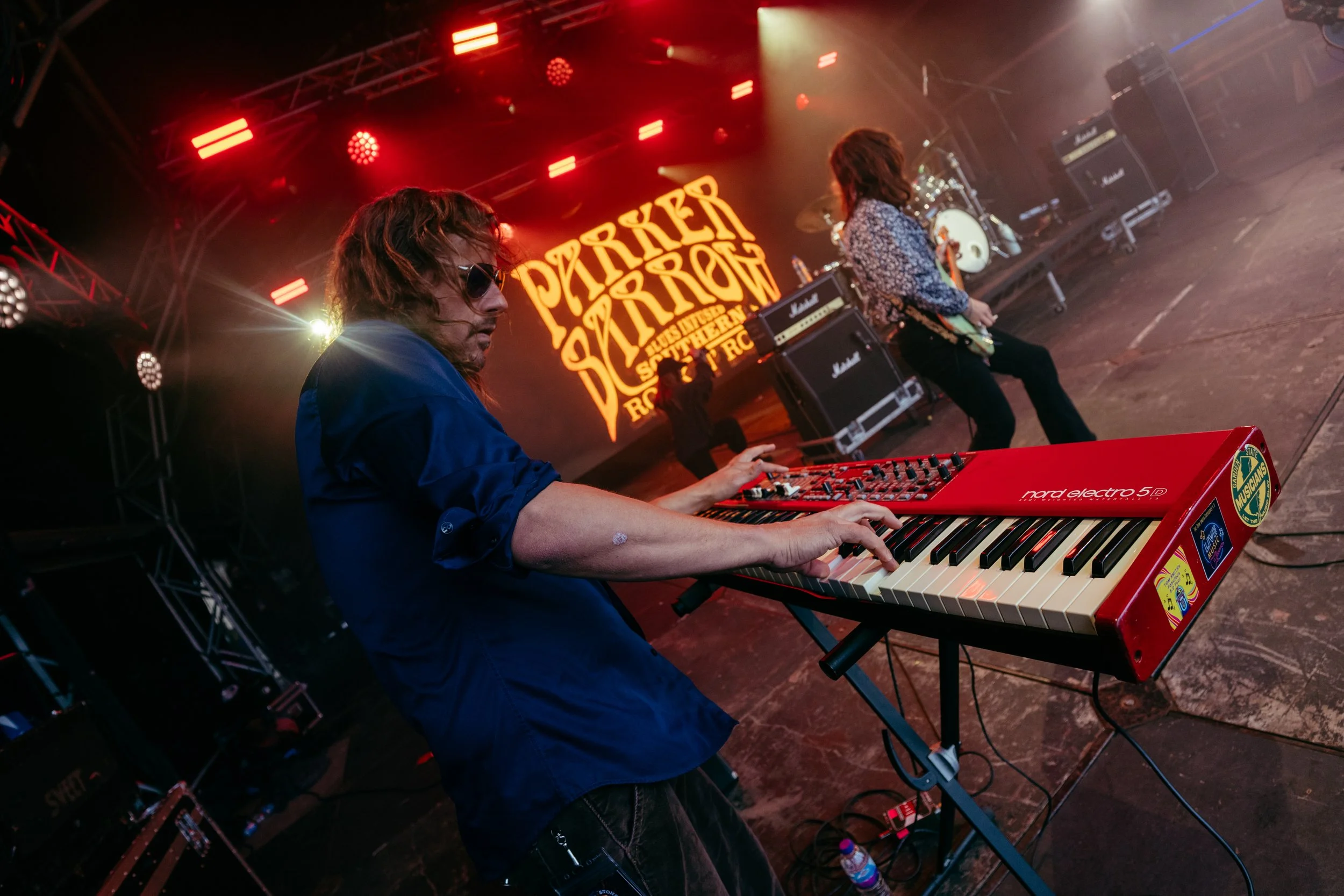 Musician playing red keyboard on stage with band playing in the background at Rock & Roll event.
