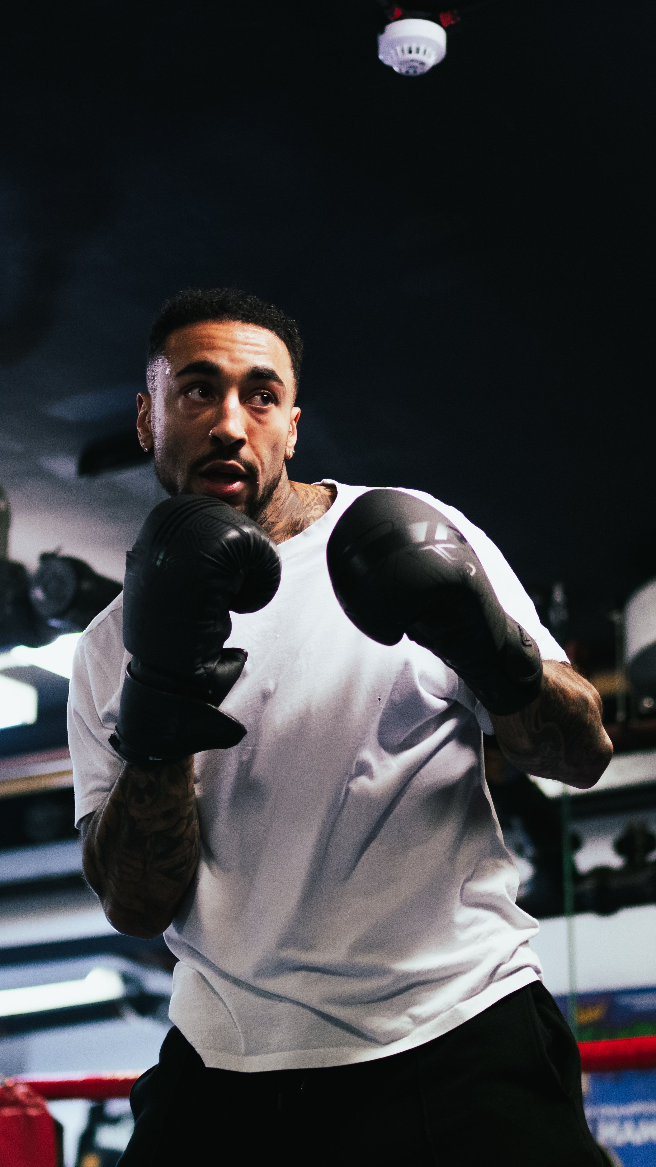 A man in white t-shirt wearing boxing gloves practicing boxing in a gym.