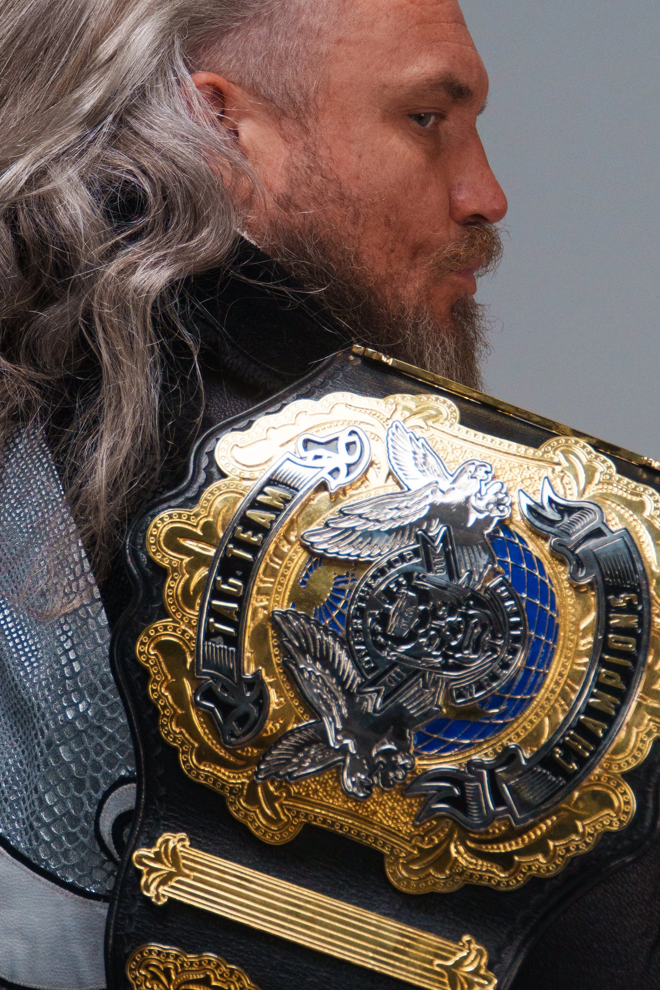 A bearded man with long gray hair wearing a black shirt, holding a championship belt with the words 'STREET TEAM' and 'CHAMPION' visible.