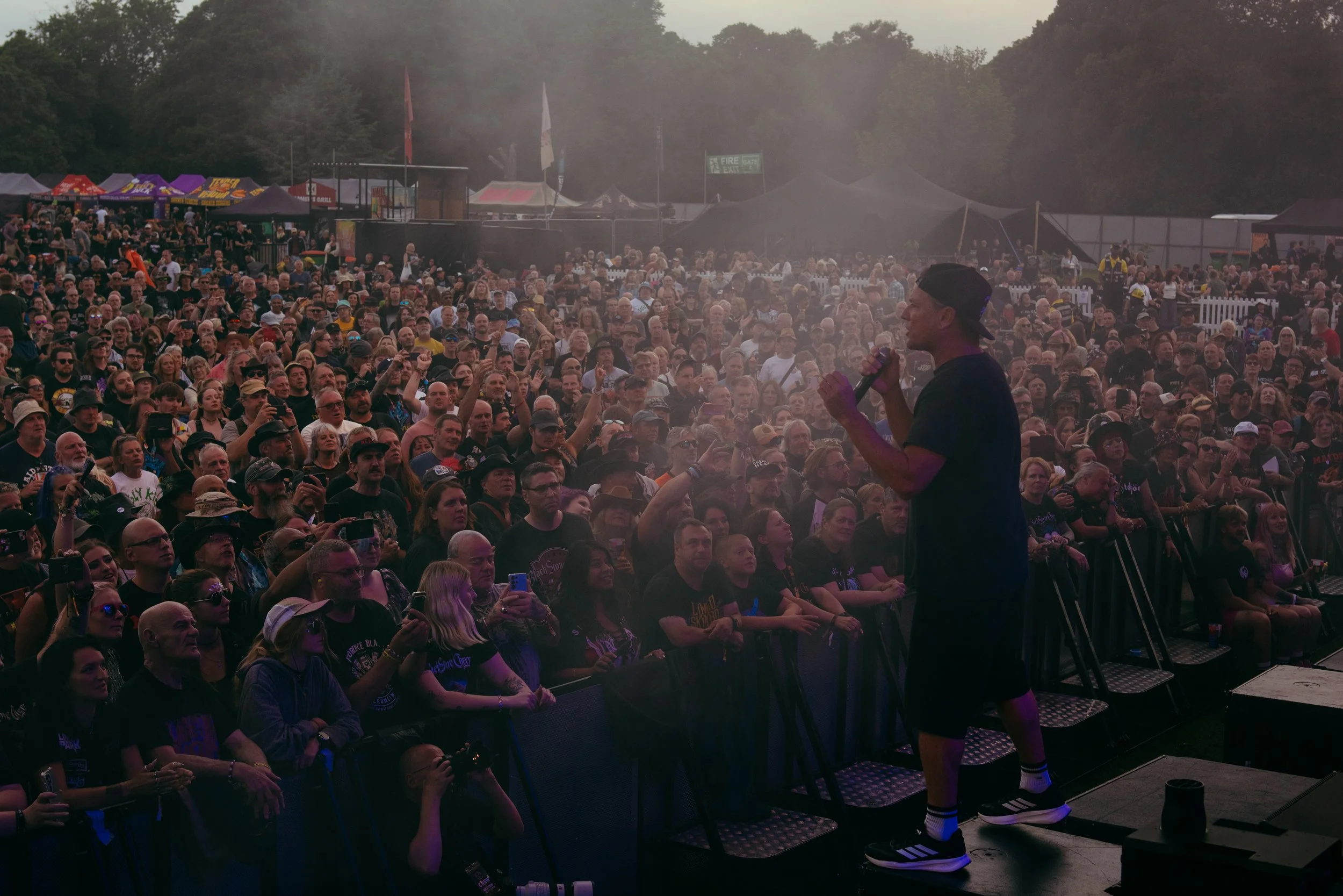 A performer singing into a microphone on stage at a large outdoor concert with a crowd of fans watching.