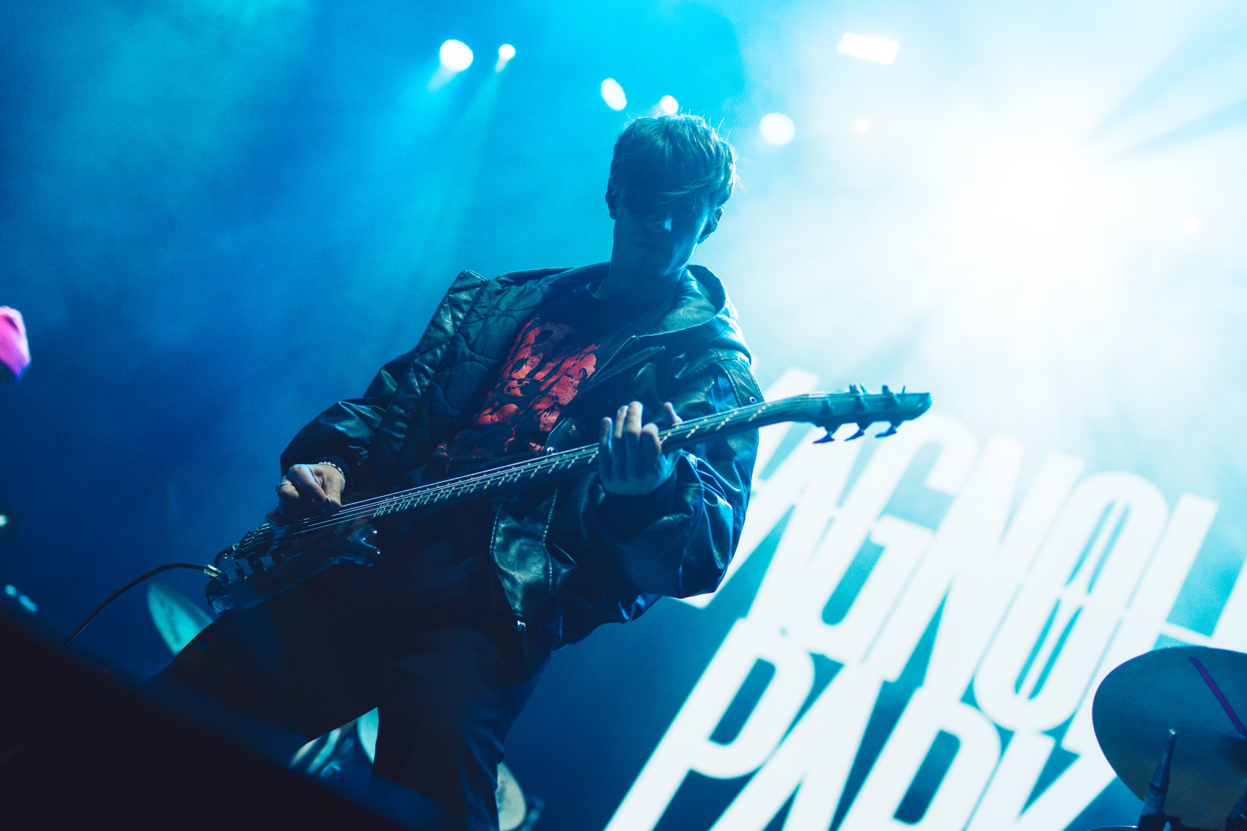 A musician playing an electric guitar on stage with bright blue lighting and a large illuminated background sign.