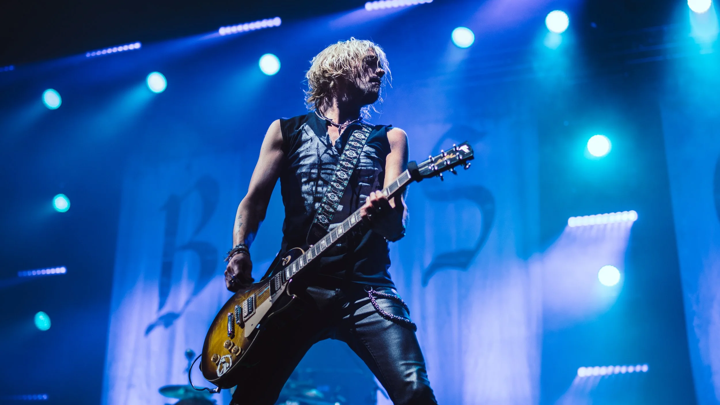 Music performer playing electric guitar on stage with blue and purple lighting.
