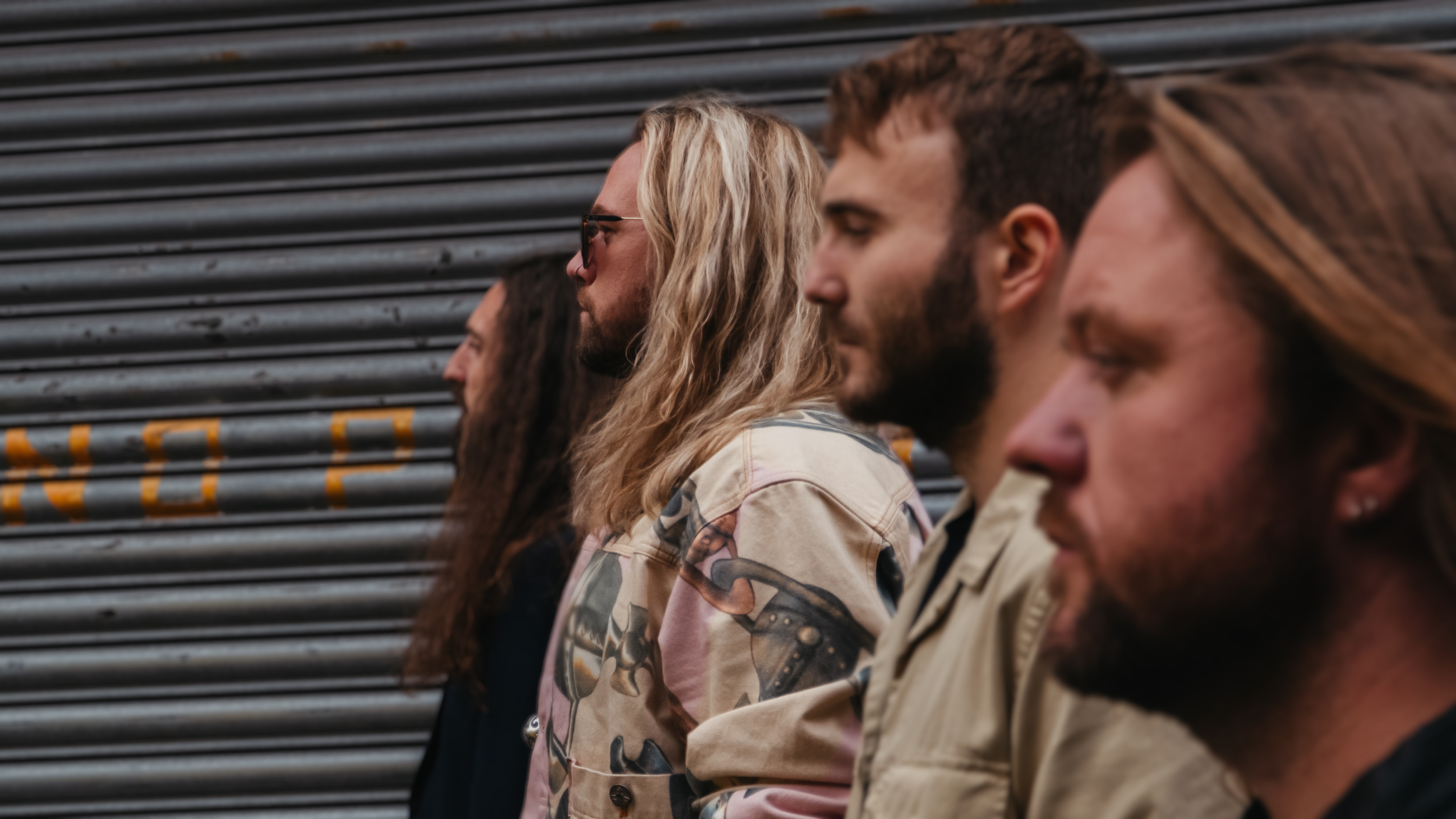 Four people standing in profile against a metal roller shutter background.