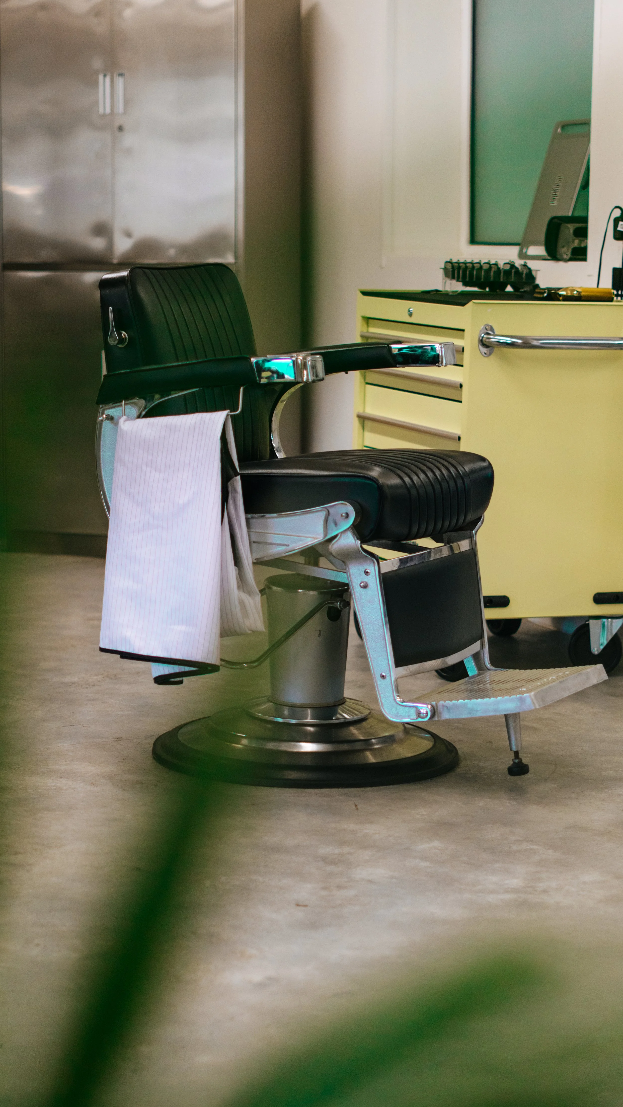 An empty vintage barber chair with black leather upholstery and chrome details in a modern barbershop or salon.