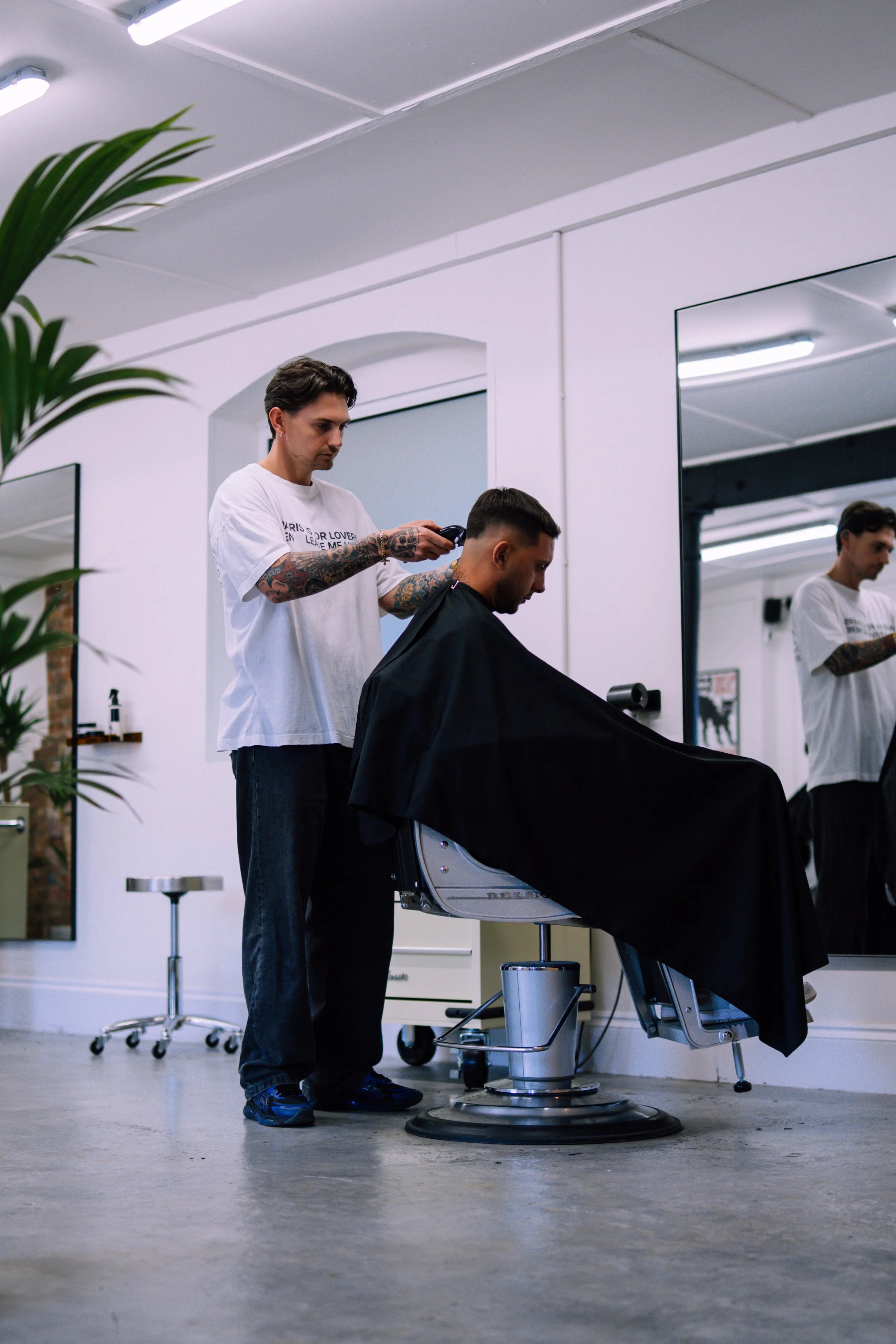 Barber giving a haircut at a modern salon with large mirror and white walls.