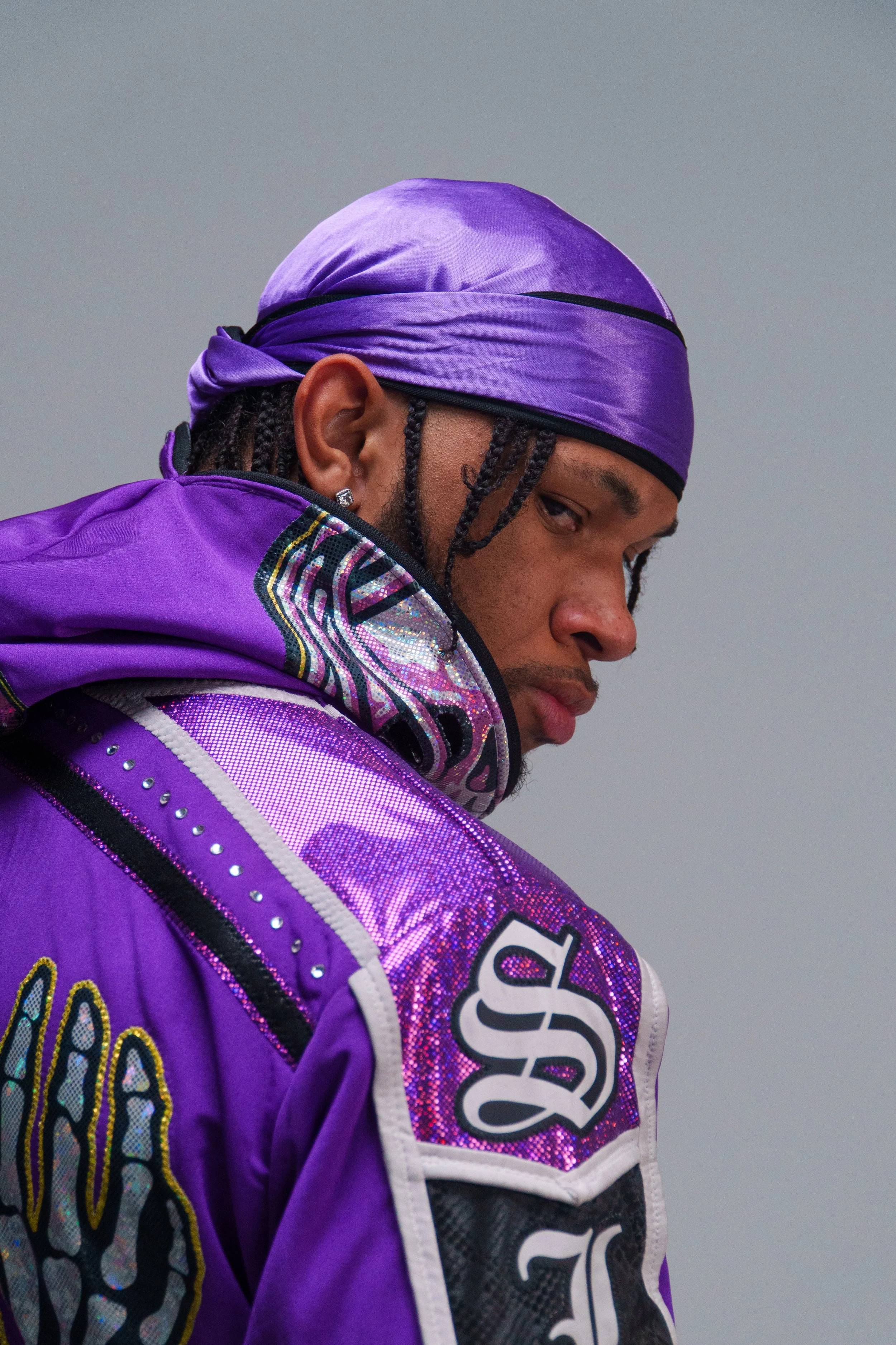 Close-up of a person wearing a purple racing suit and a purple headscarf, with braided hair, looking over their shoulder