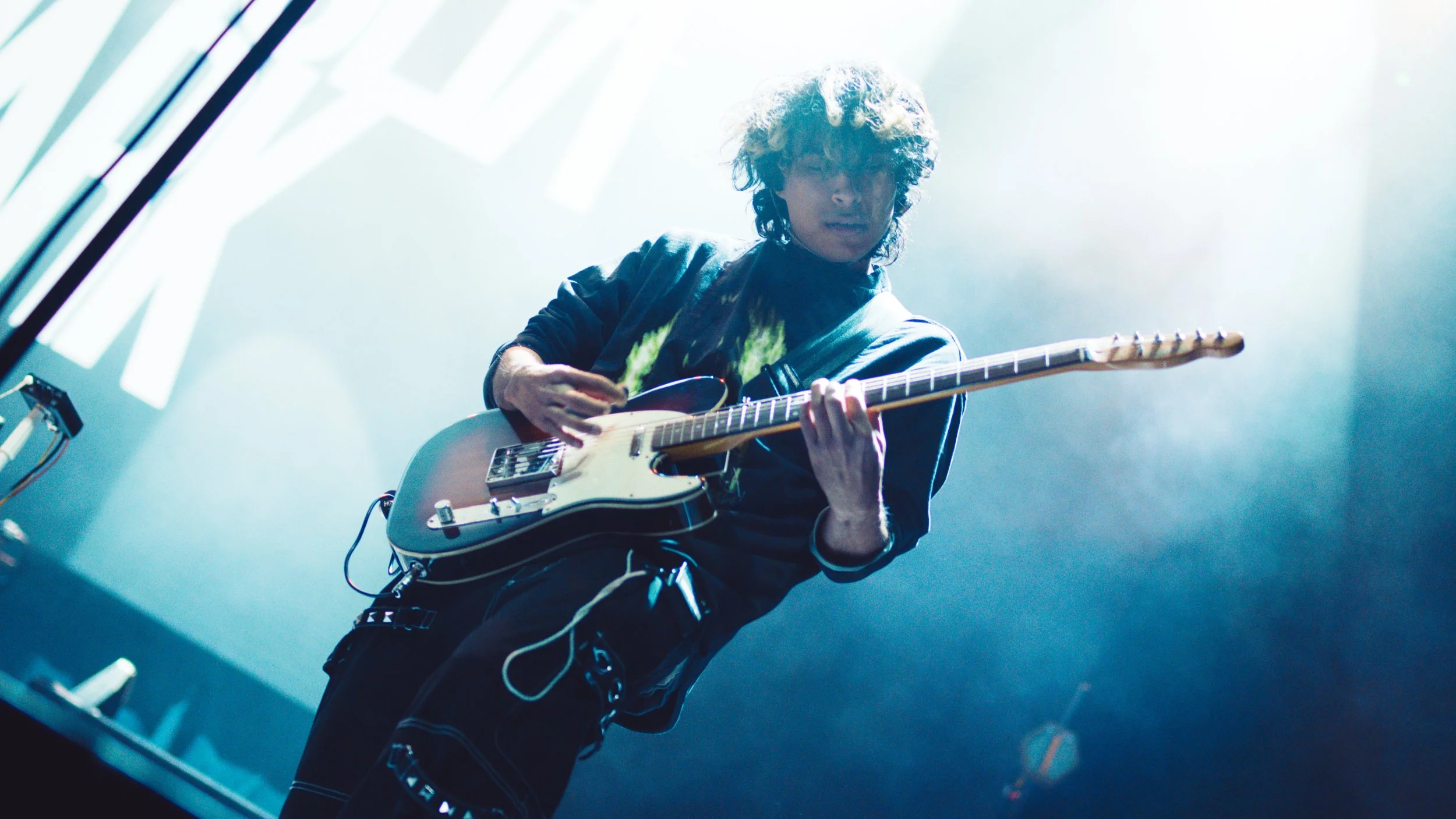 A guitarist performing on stage with bright stage lighting.