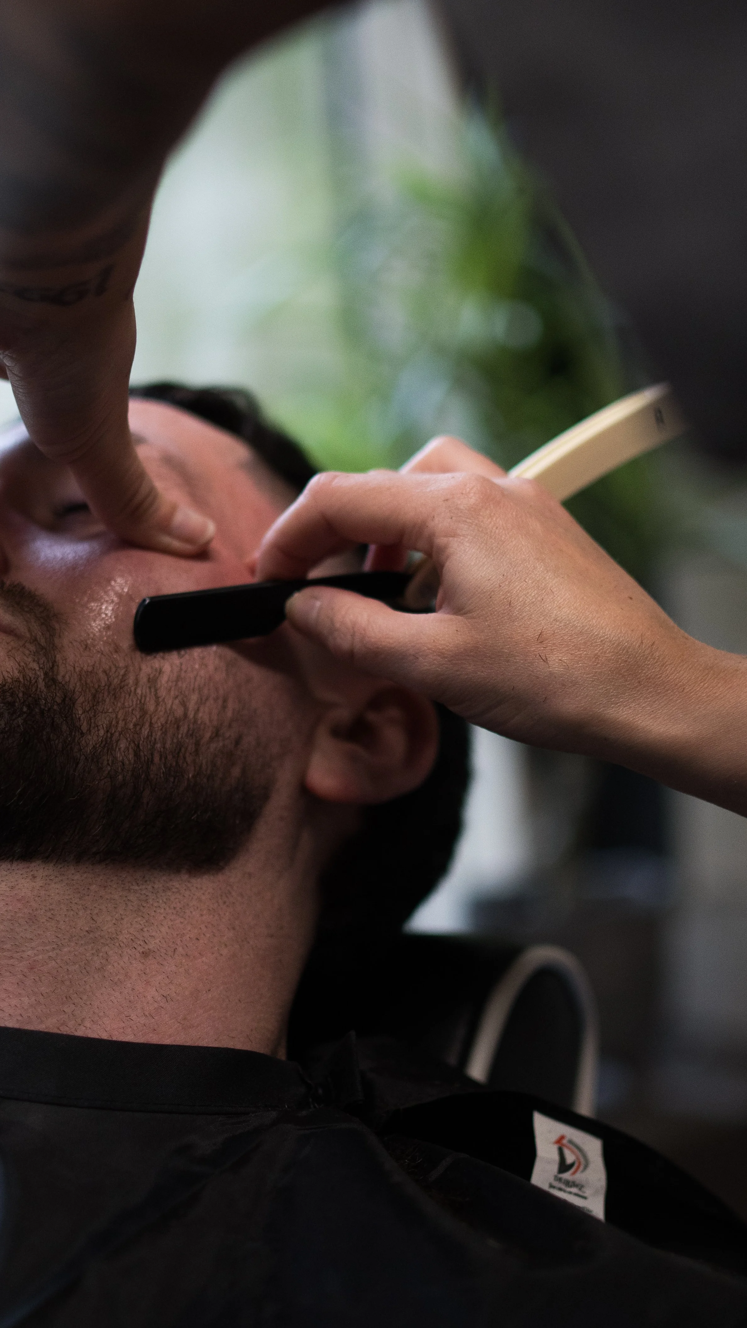 A person receiving a shave with an electric razor while lying down, with a barber or stylist shaving their face.