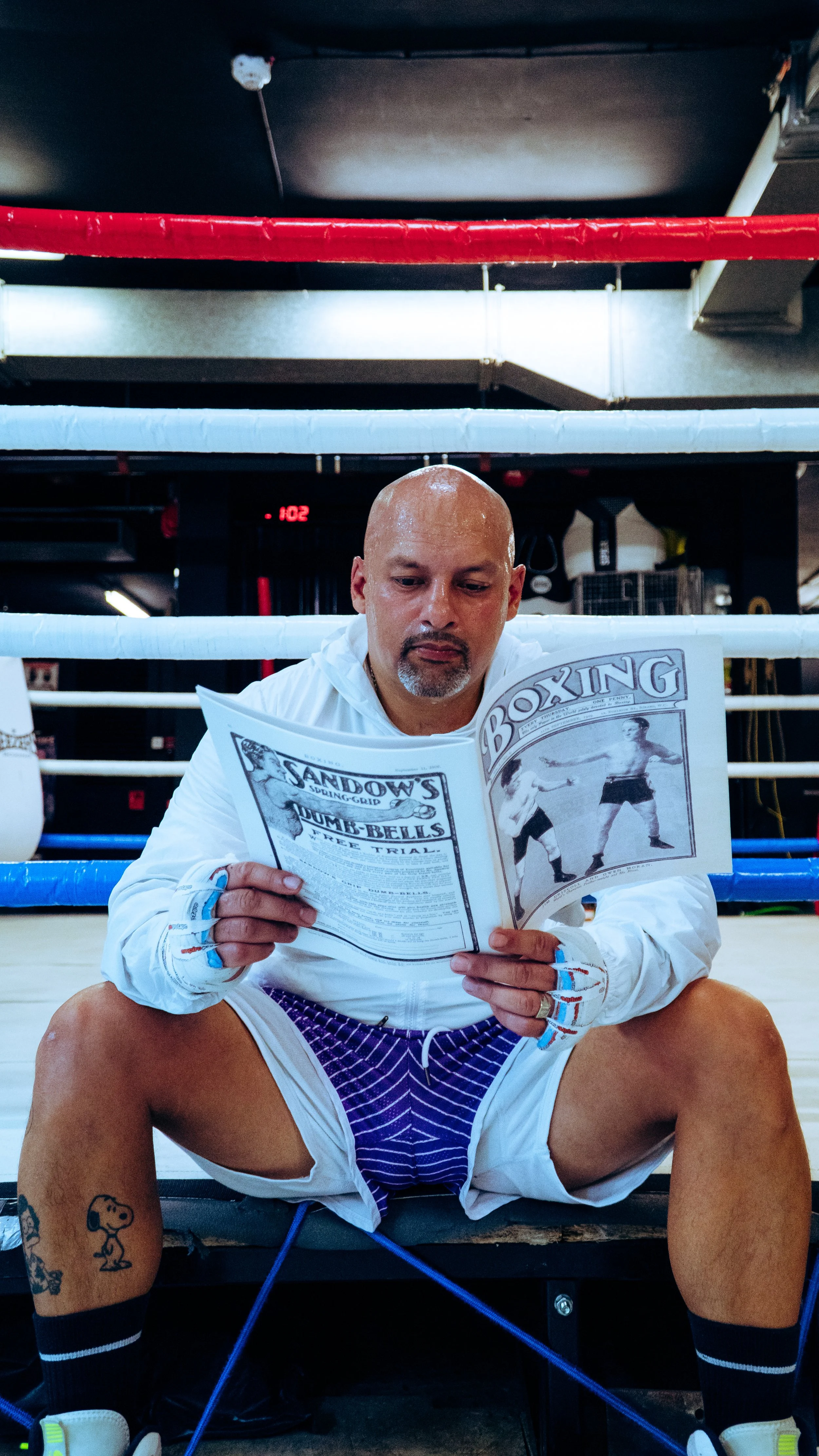 A man sitting in a boxing ring reading a vintage boxing magazine.