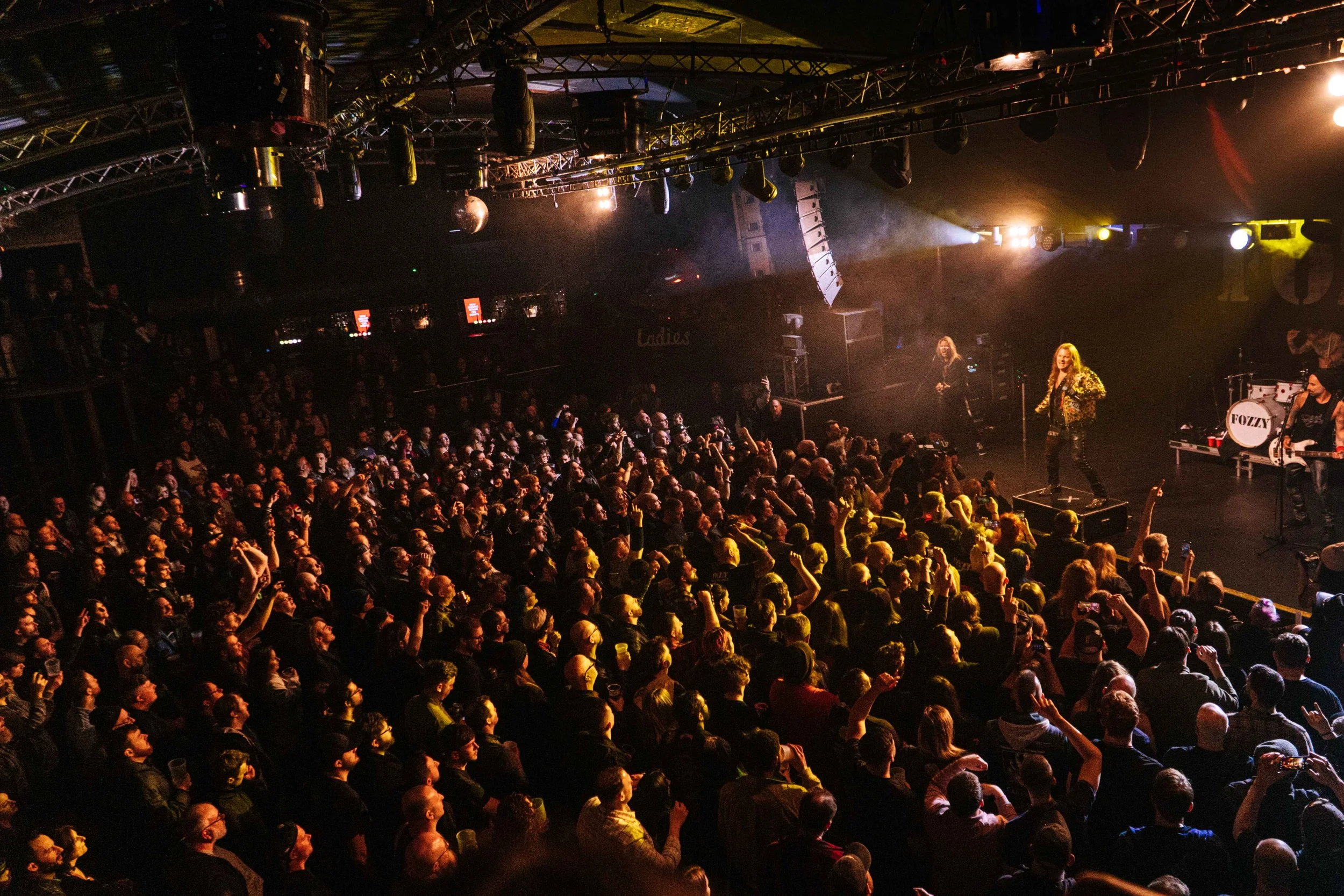 Crowd of people watching a live music performance on stage with bright lights and musical instruments.