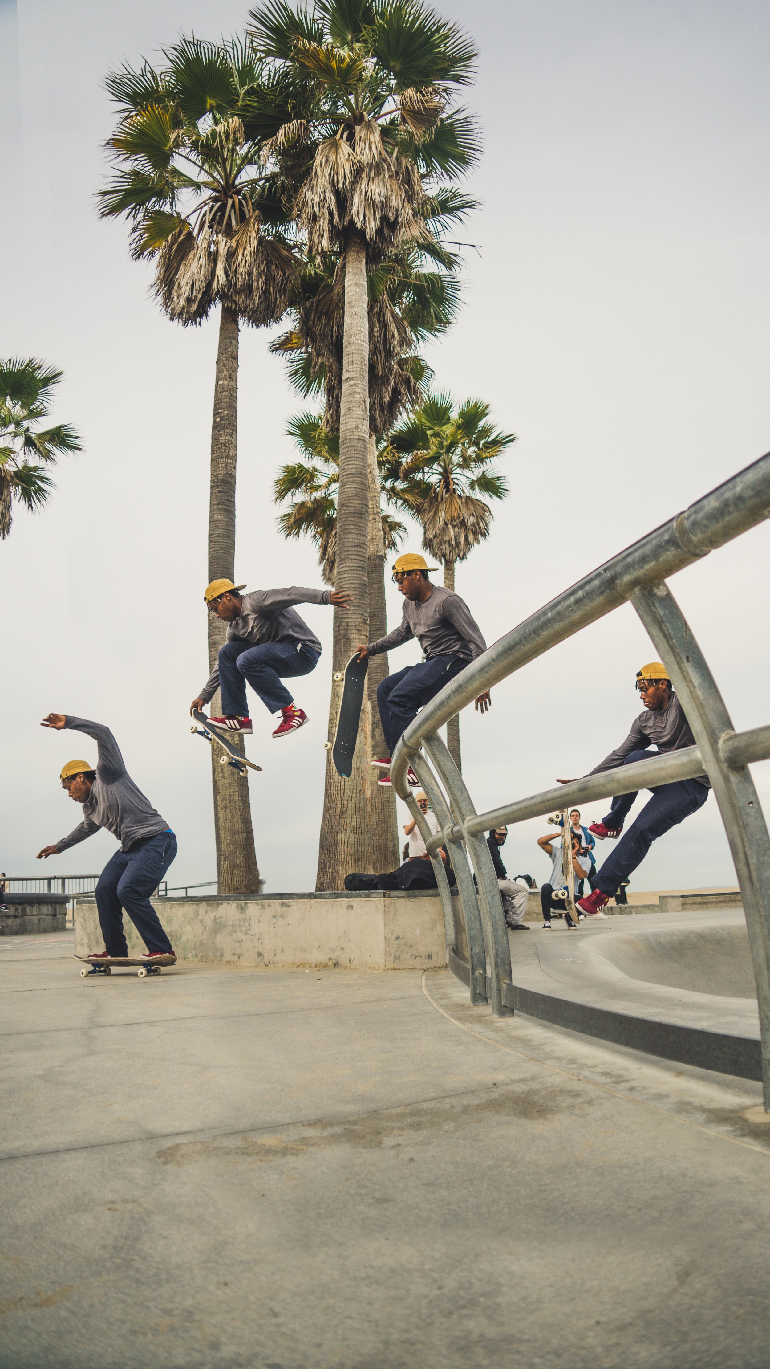 Skateboarders performing tricks at a skatepark with palm trees in the background.
