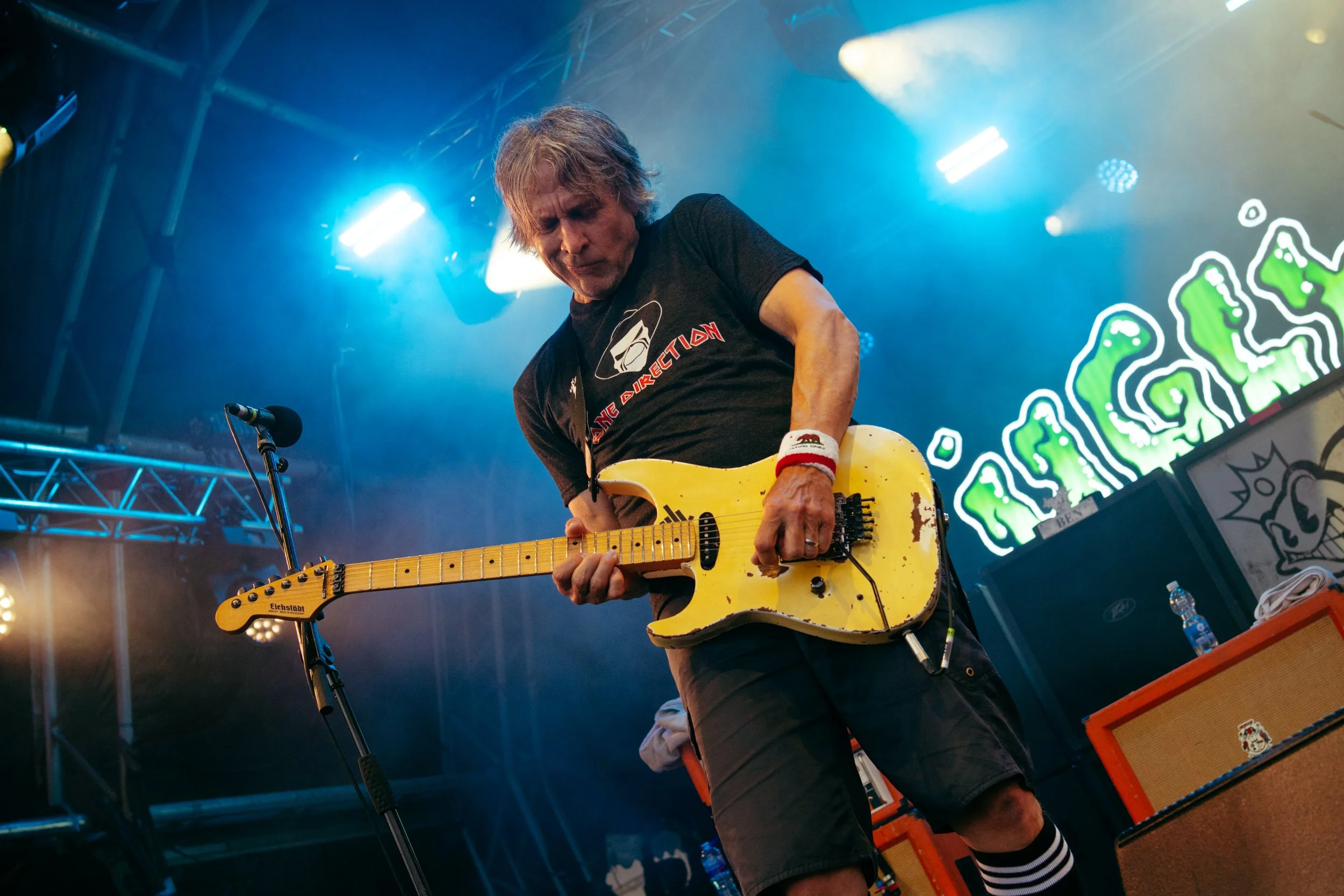 A musician playing an electric guitar on stage with colorful lighting and decorative background elements.