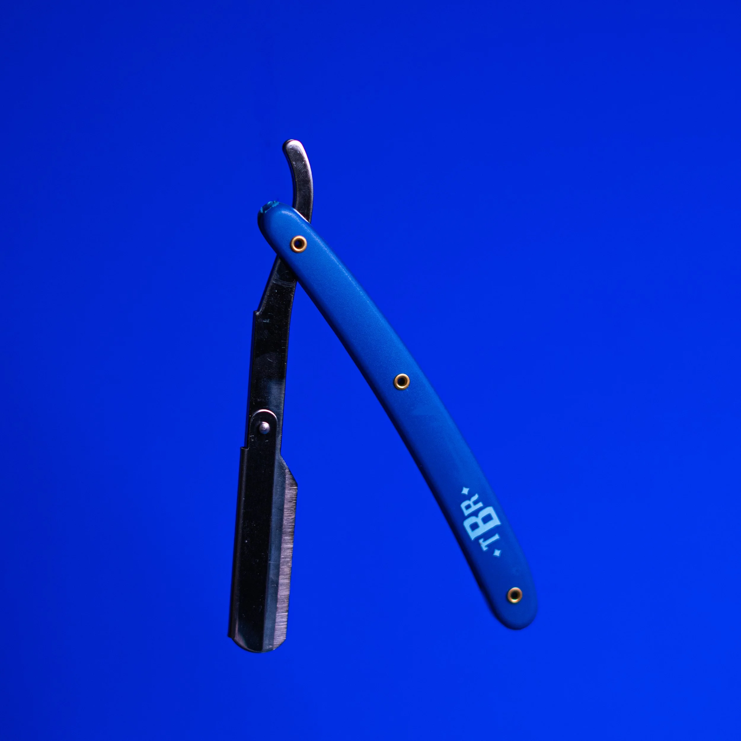 Straight-razor with a blue handle and the word "TRB" on it, floating against a blue background.