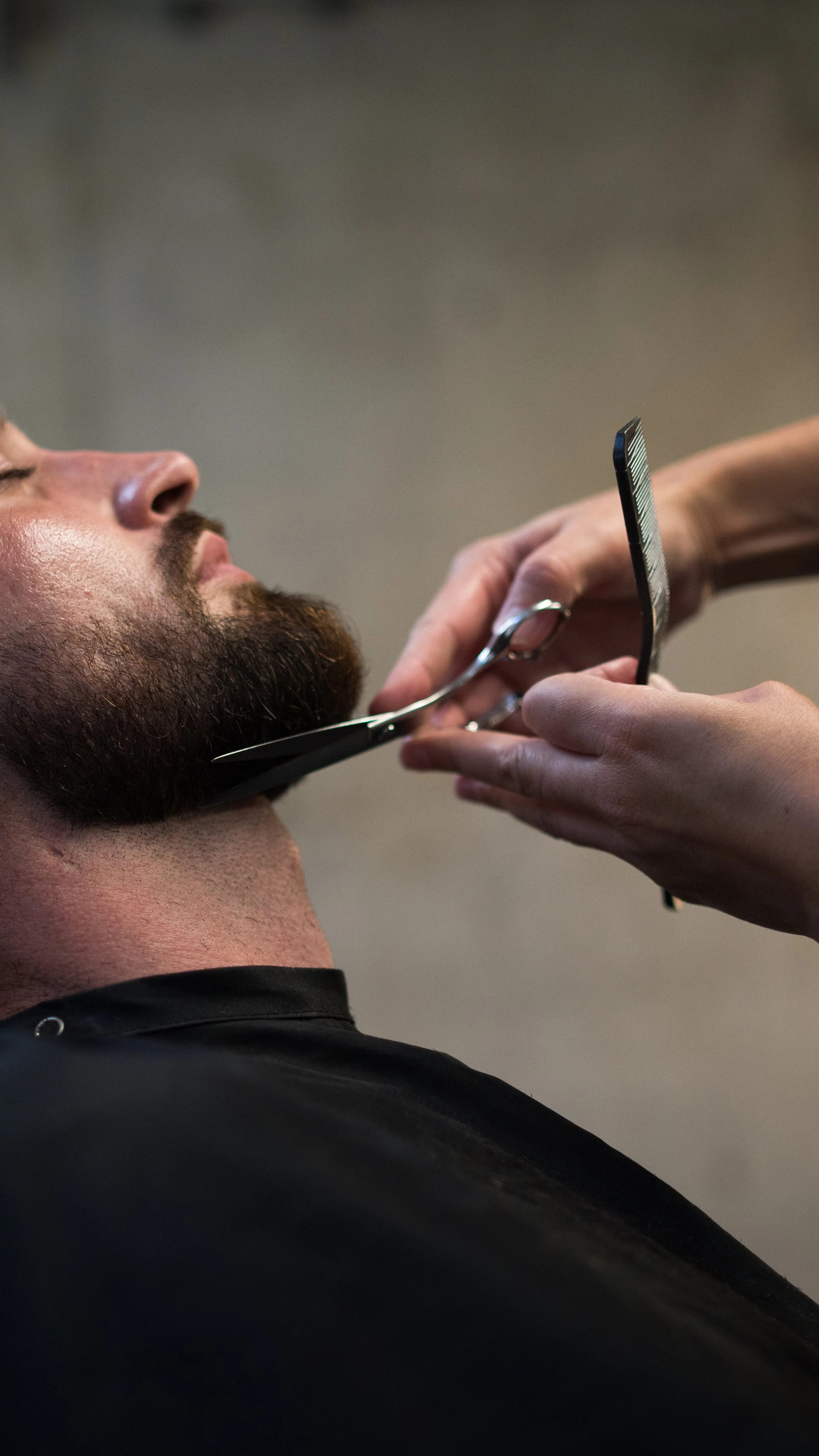 A person getting a beard trim at a barbershop, with the barber using scissors and a straight razor on the man's beard.