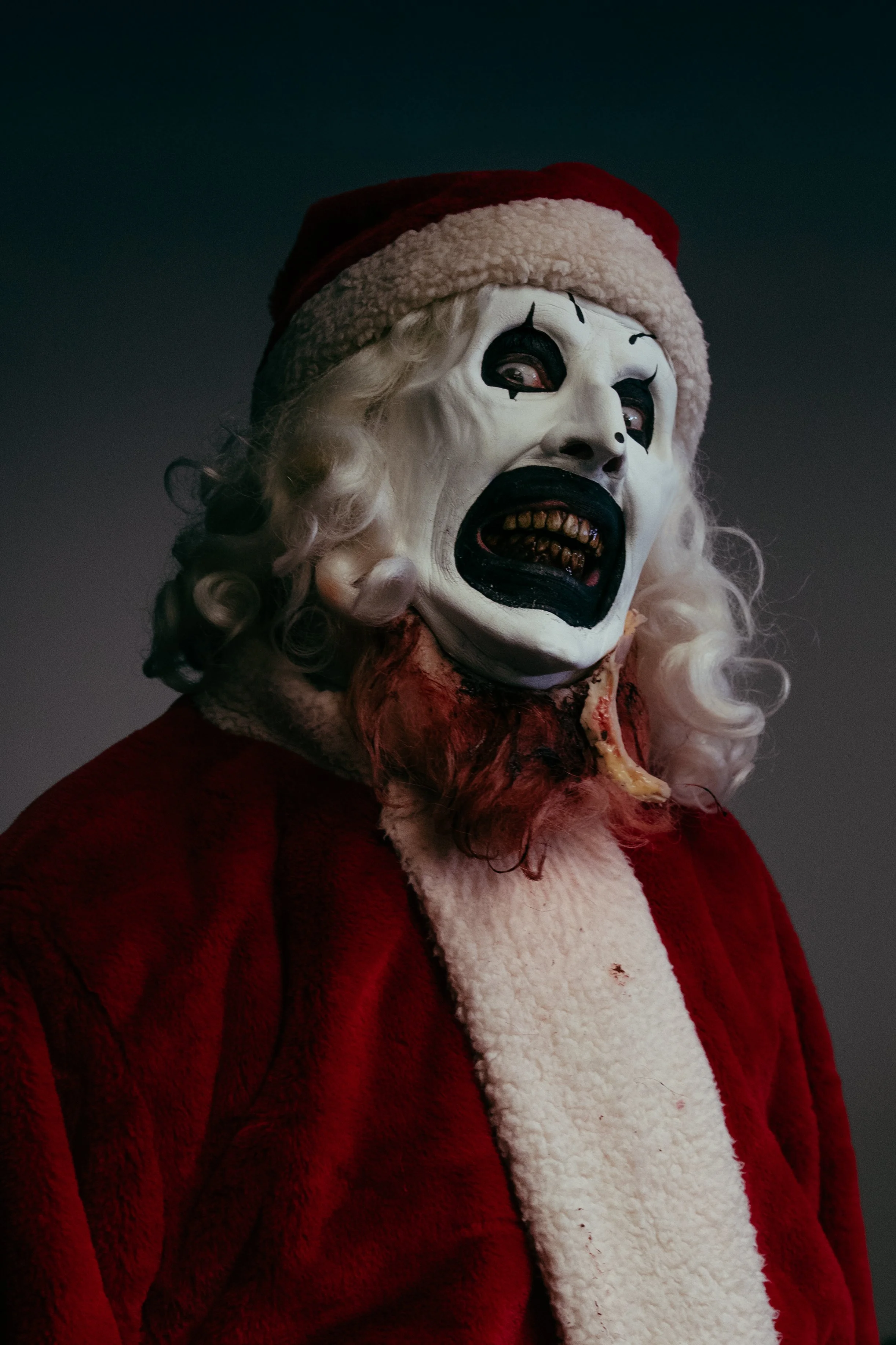 A creepy clown dressed as Santa Claus with a sinister, decayed face and a Santa hat.